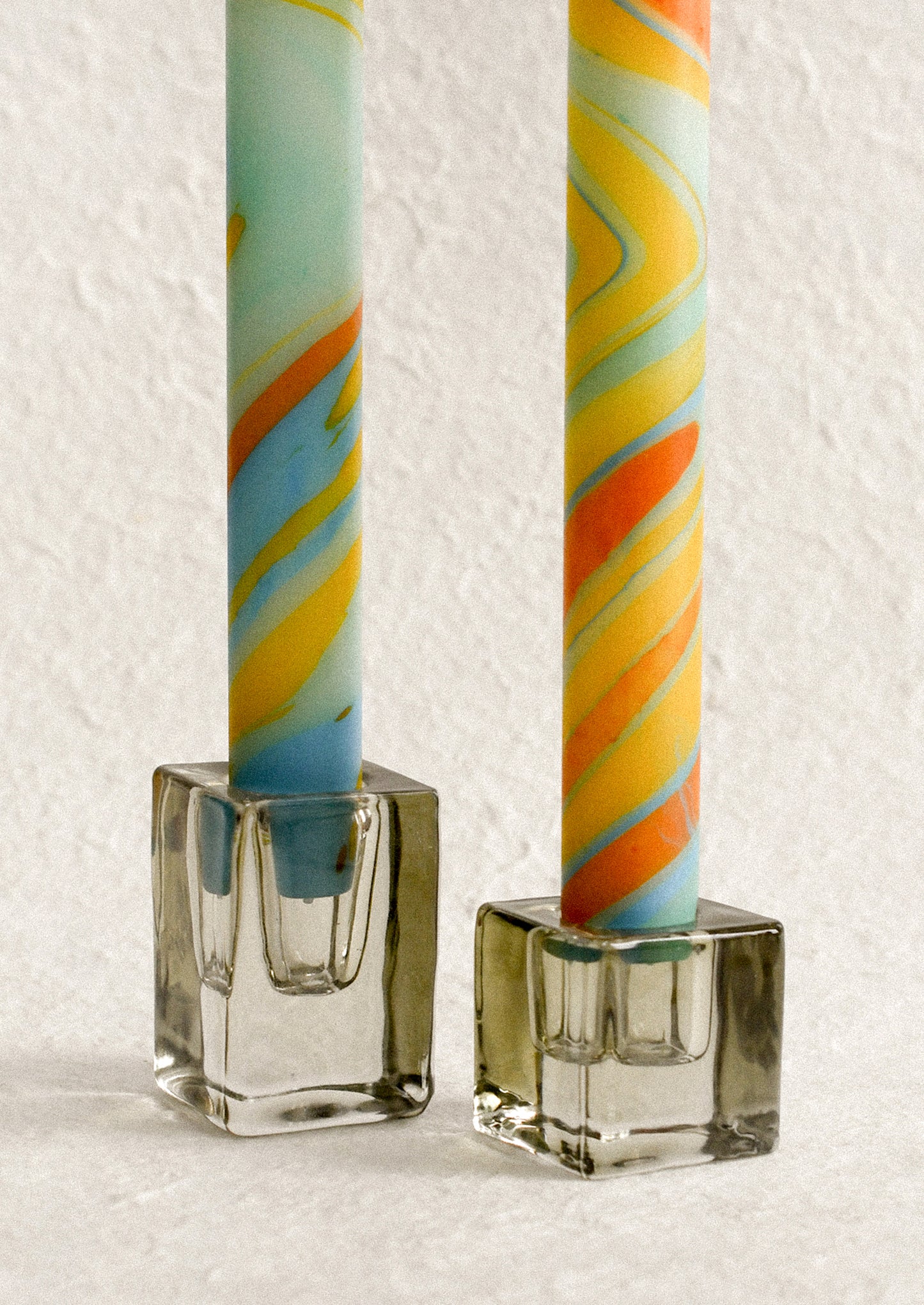 A marbled taper candle in blue, orange and yellow swirl pattern.