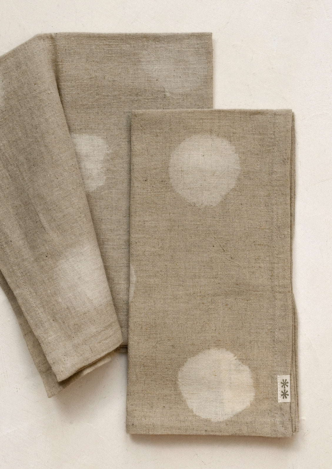 A pair of natural colored napkins with polka dot resist pattern.