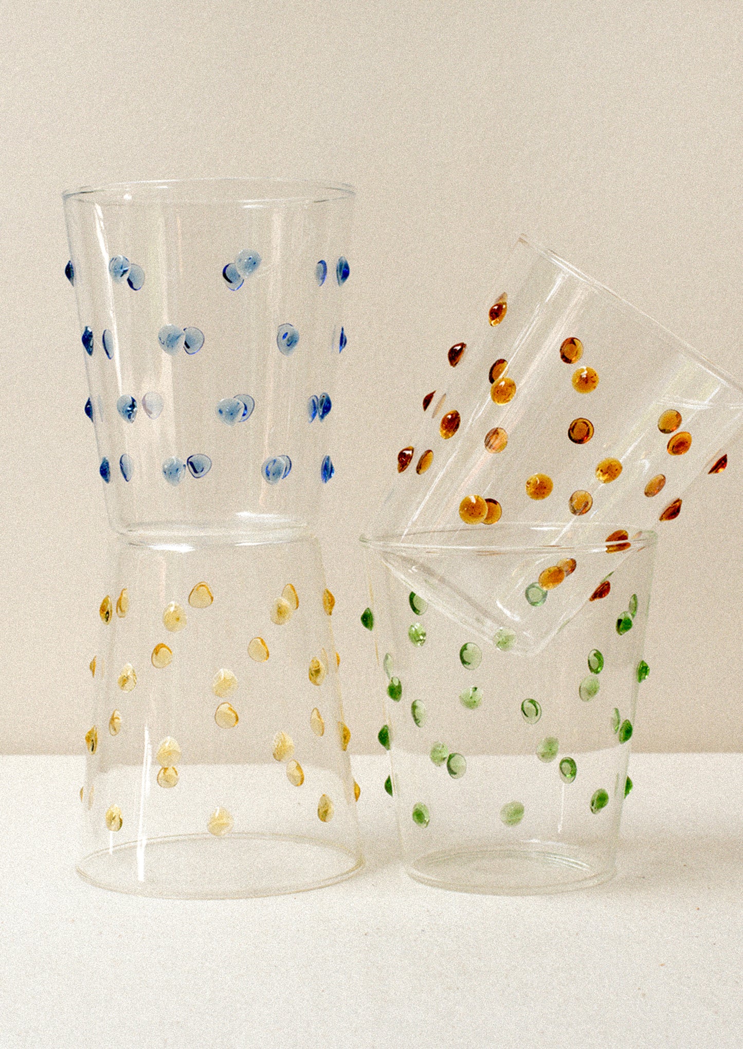 Four clear glass tumblers with textured raised dots on outside, in four color options.
