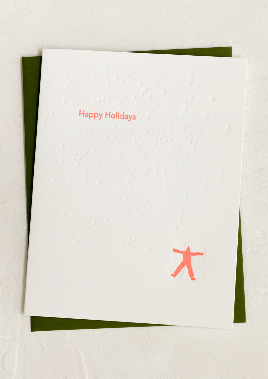 White letterpress greeting cards with neon 'Happy Holidays' text and red silhouette of a person making snow angels.