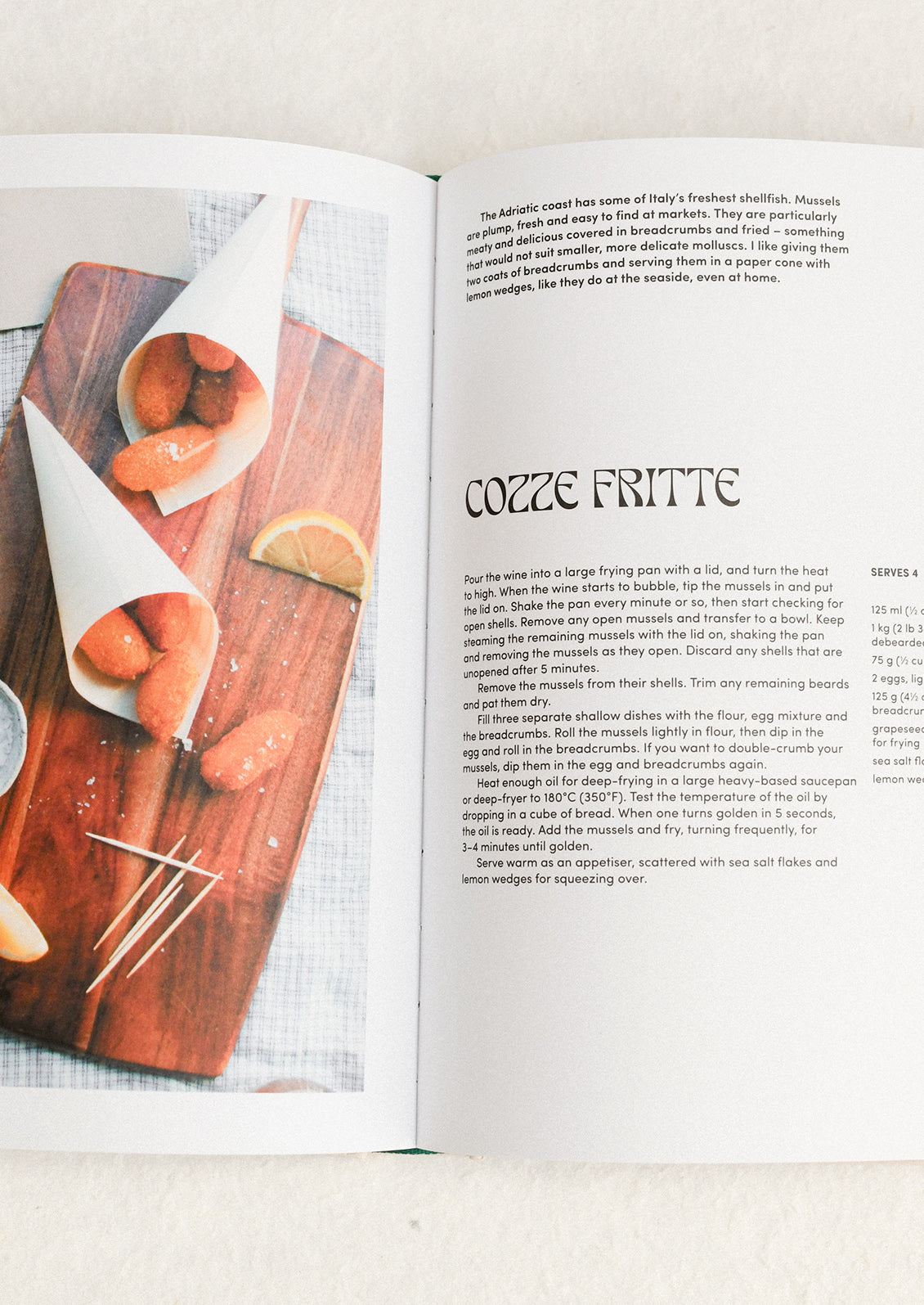 Open cookbook showing a recipe for Cozze Fritte with a wooden board and ingredients.