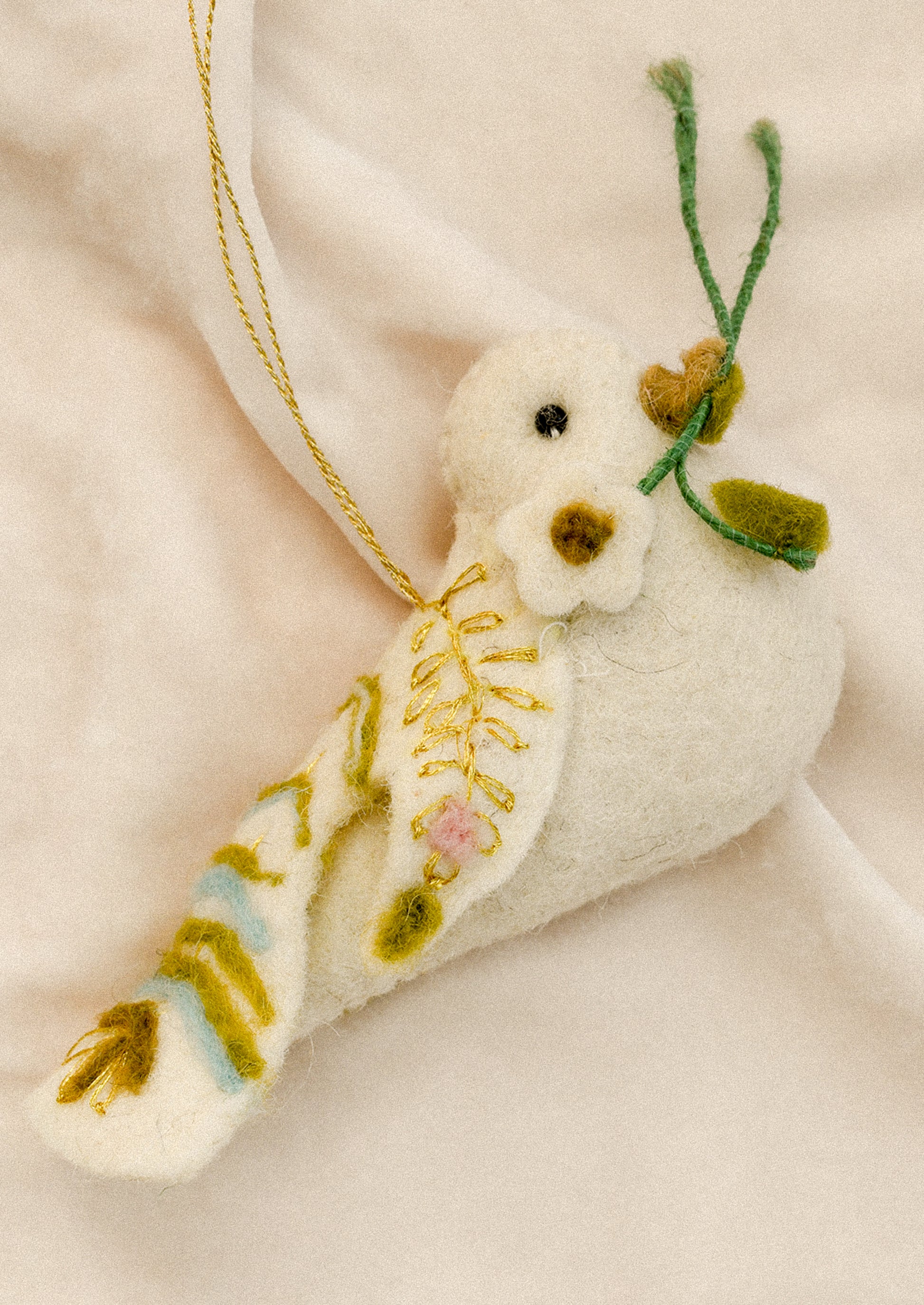 A felted white ornament depicting a dove holding a sprig in its beak, with decorative pastel embroidery.
