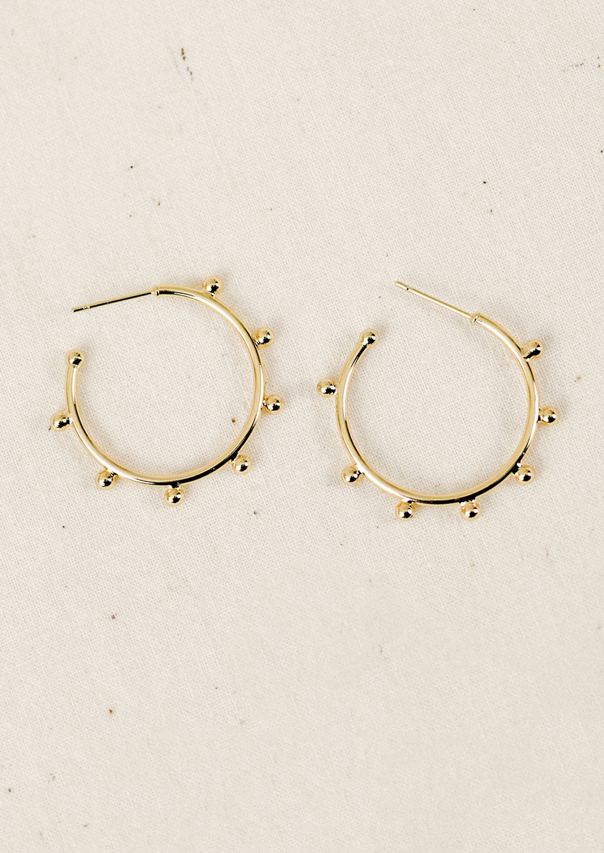 Gold hoop earrings with ball details on a beige background
