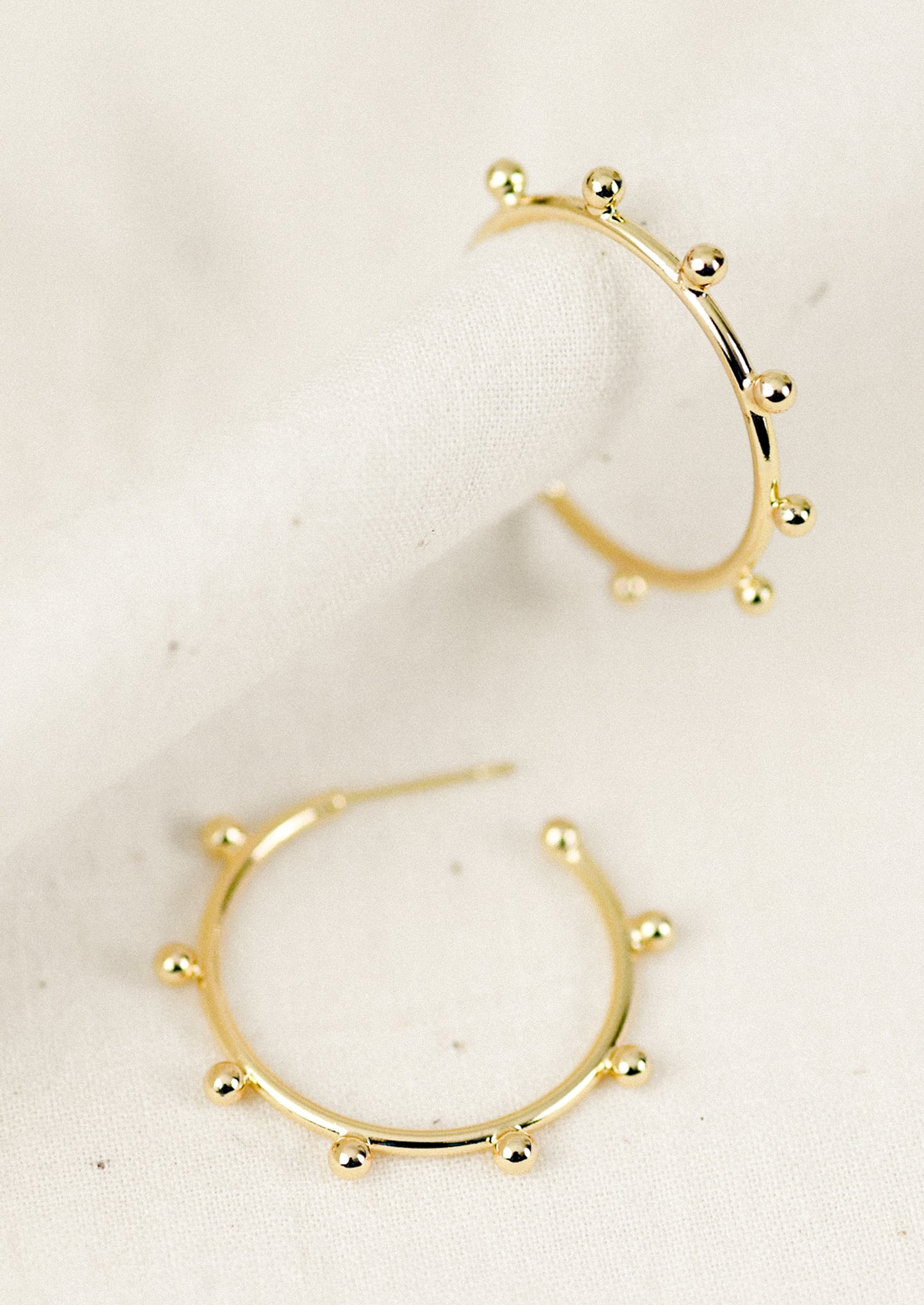 Gold hoop earrings with ball details on a beige background