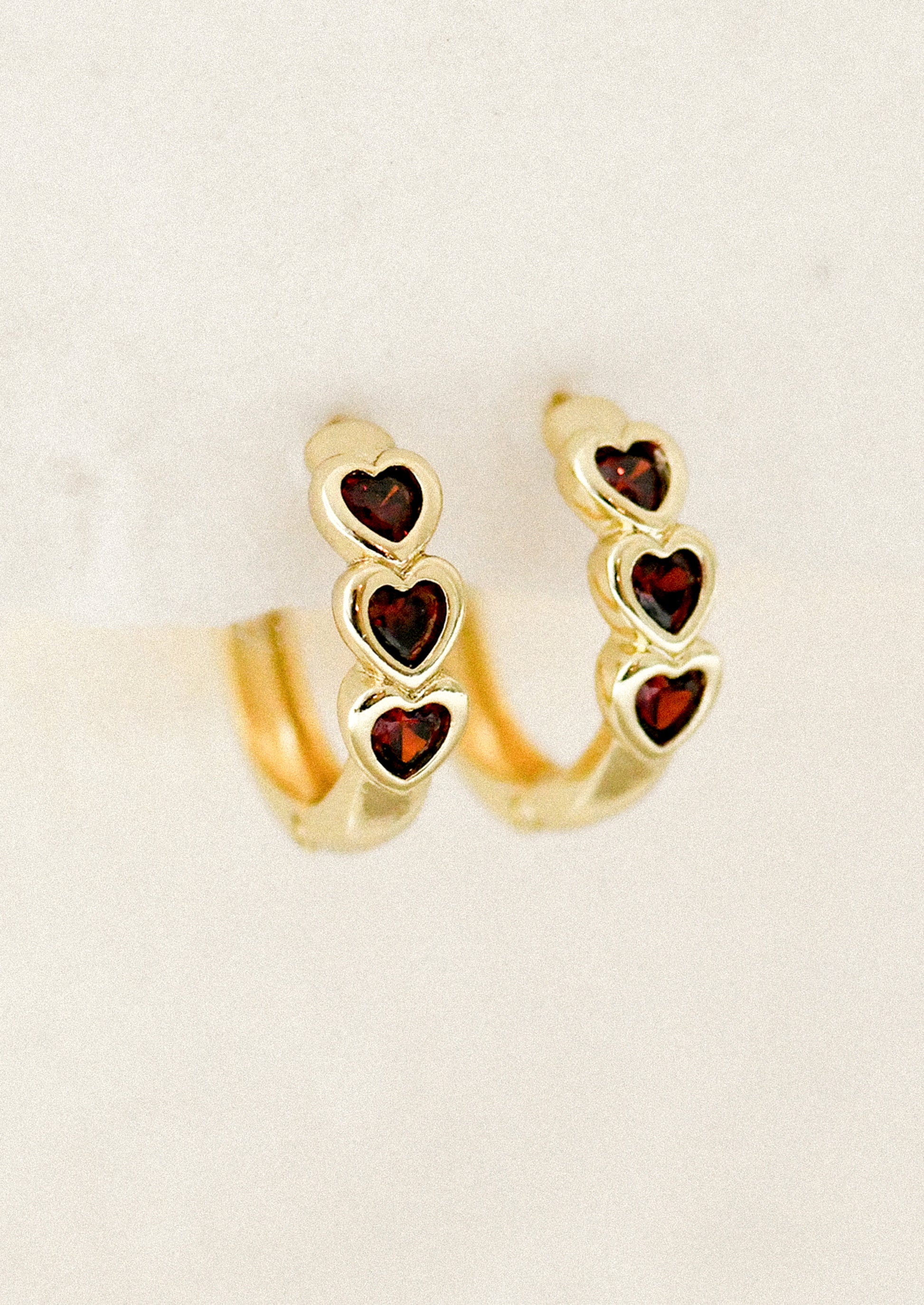 Gold hoop earrings with heart-shaped gemstones on a beige background
