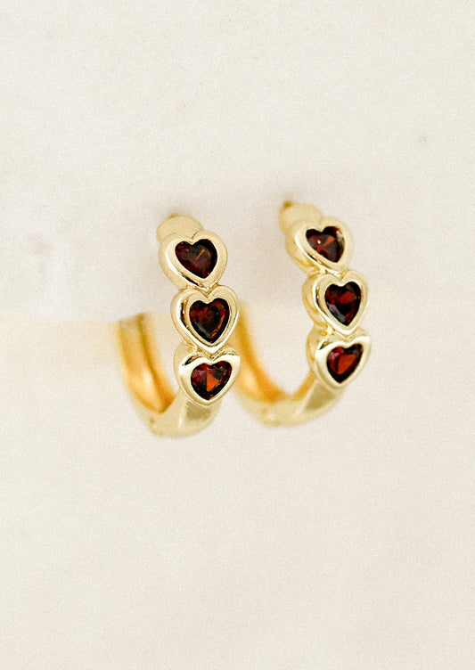 Gold hoop earrings with heart-shaped gemstones on a beige background