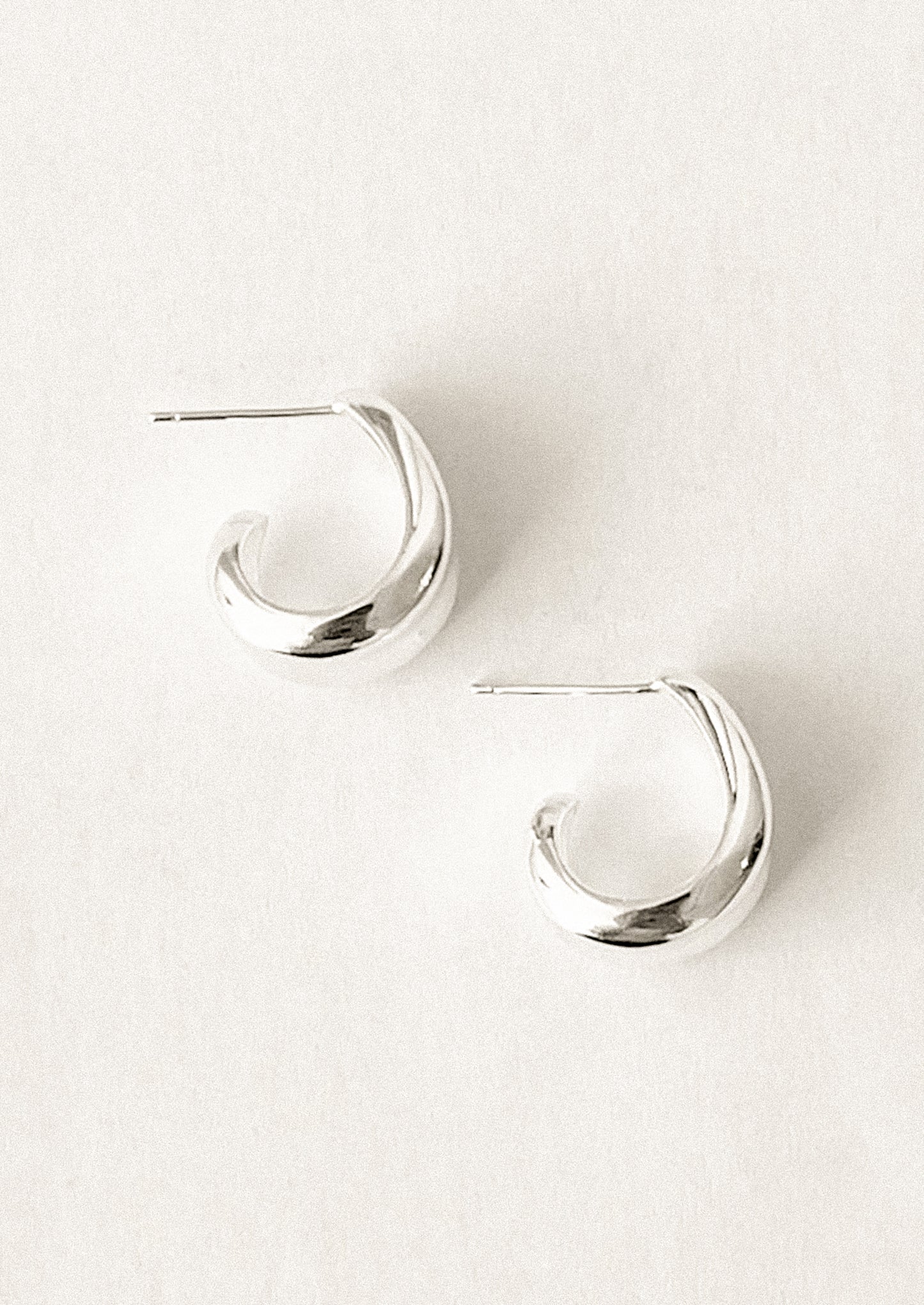 A pair of sterling silver hoop earrings with curled side detail.