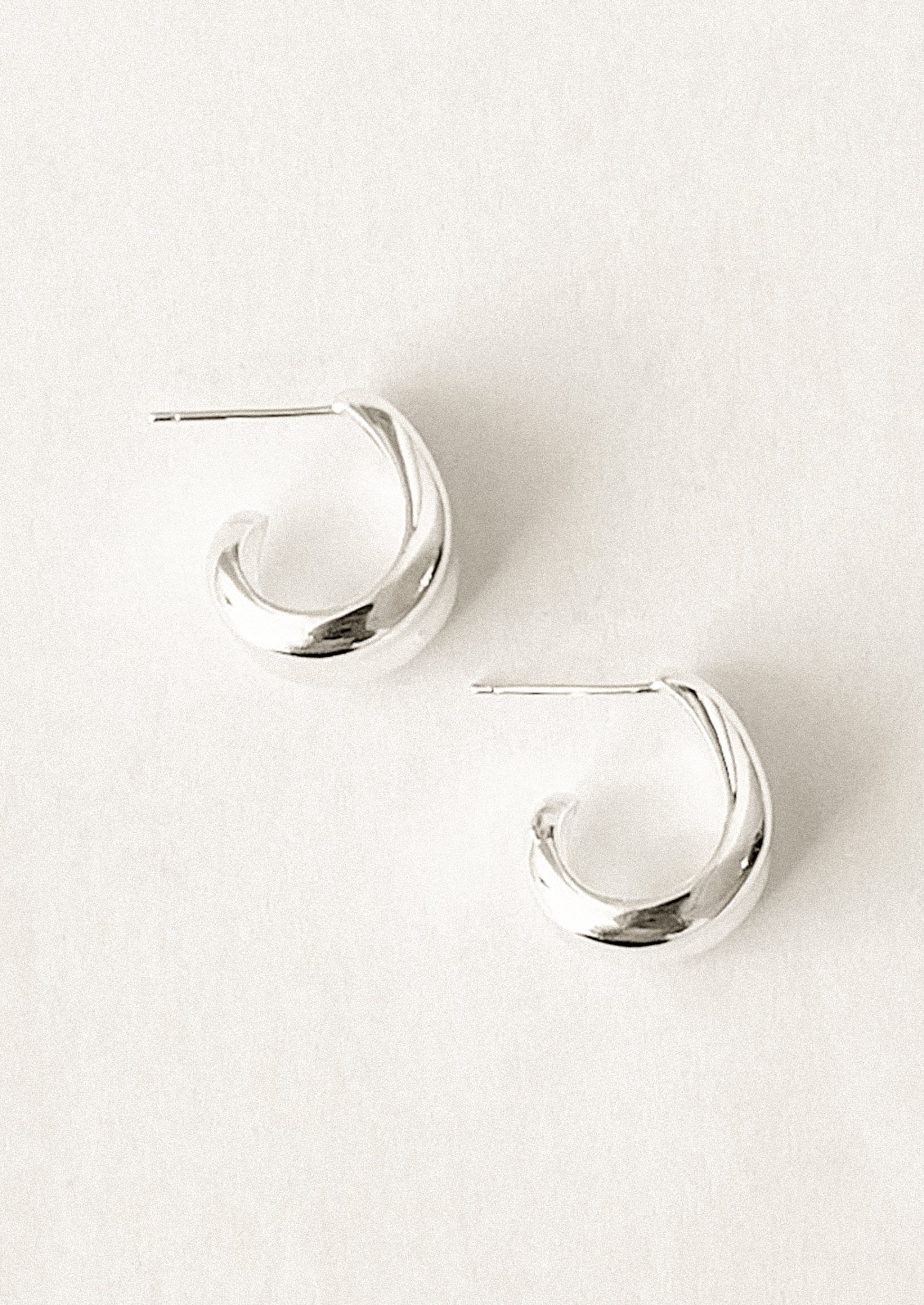 A pair of sterling silver hoop earrings with curled side detail.