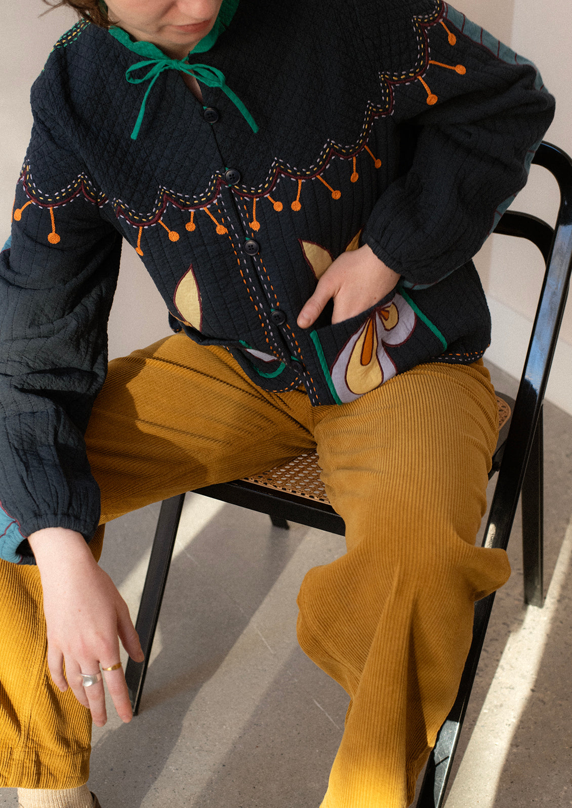 A woman wearing a navy embroidered jacket with whimsical abstract embroidery throughout.