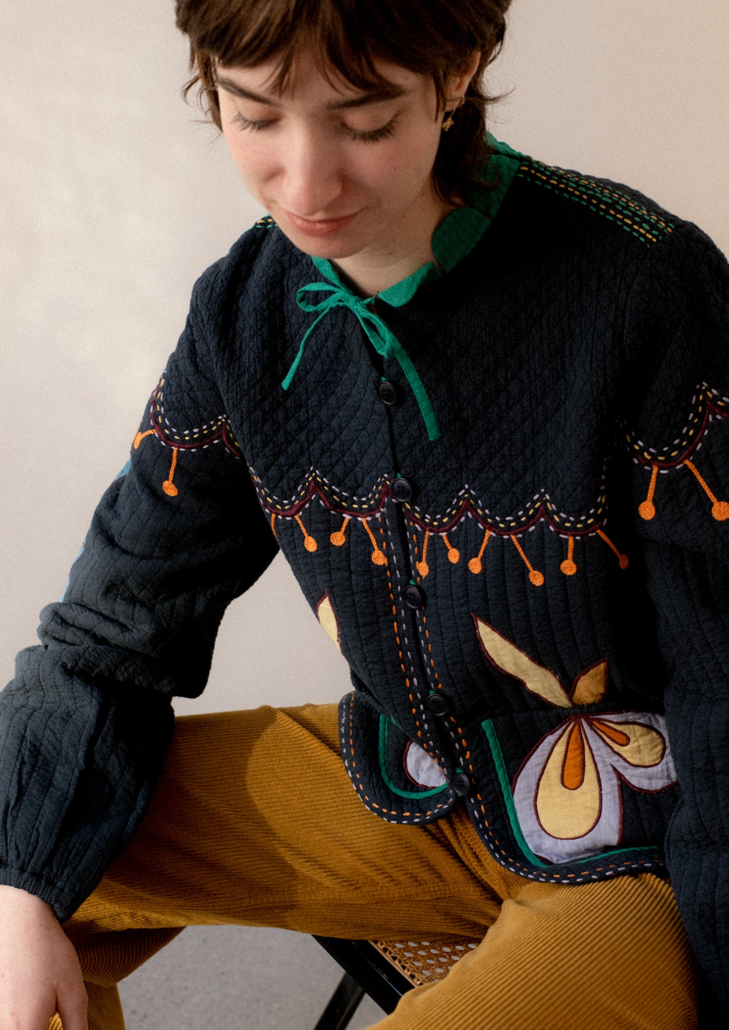 A woman wearing a navy embroidered jacket with whimsical abstract embroidery throughout.