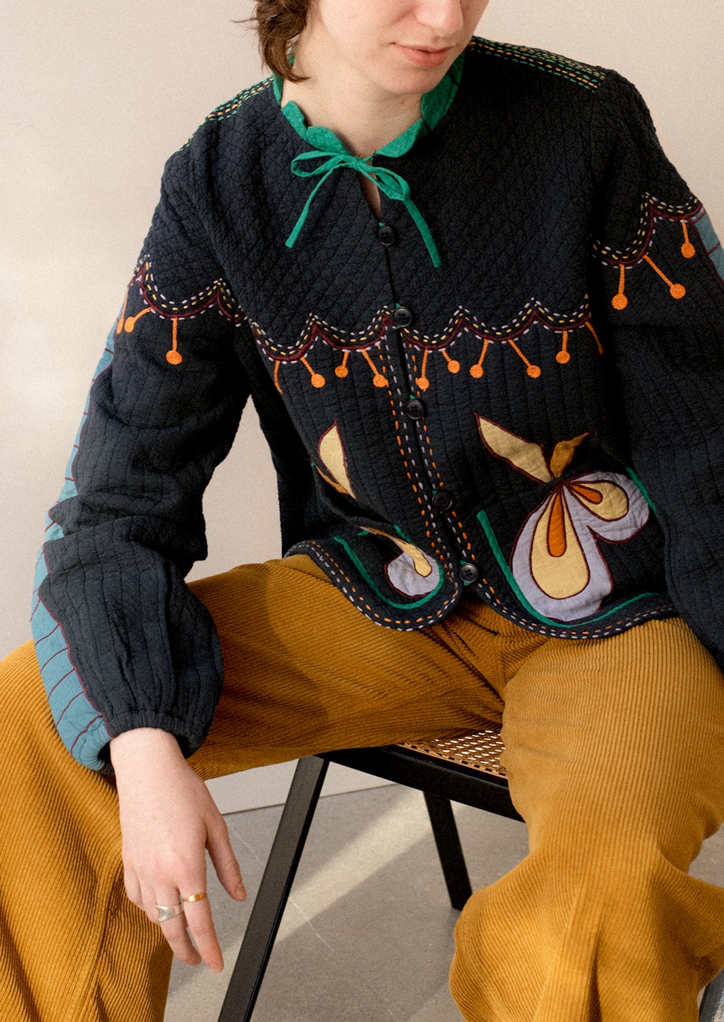 A woman wearing a navy embroidered jacket with whimsical abstract embroidery throughout.