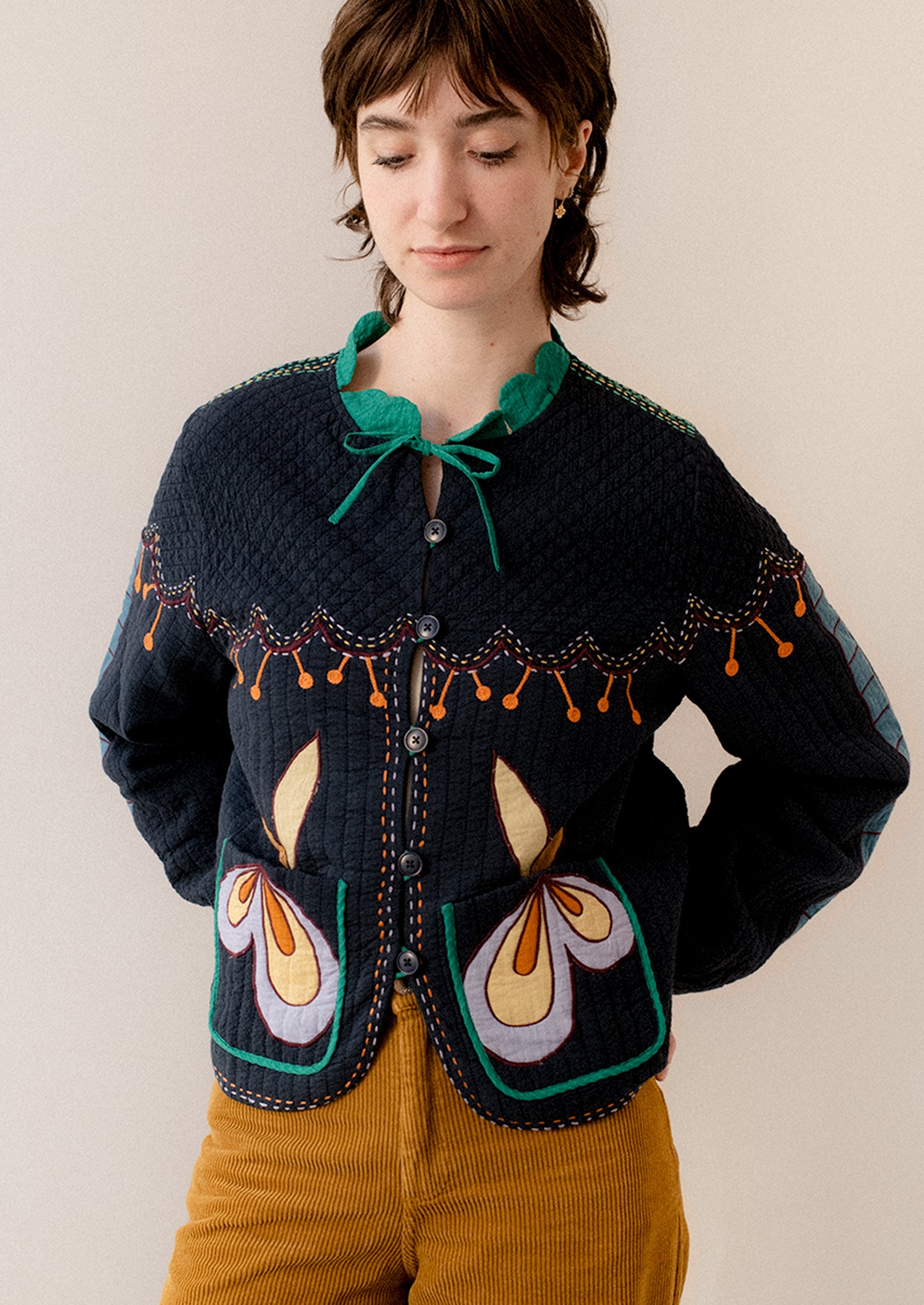 A woman wearing a navy embroidered jacket with whimsical abstract embroidery throughout.