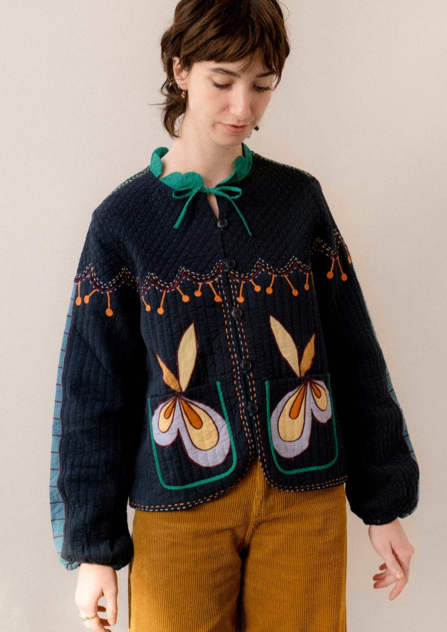 A woman wearing a navy embroidered jacket with whimsical abstract embroidery throughout.
