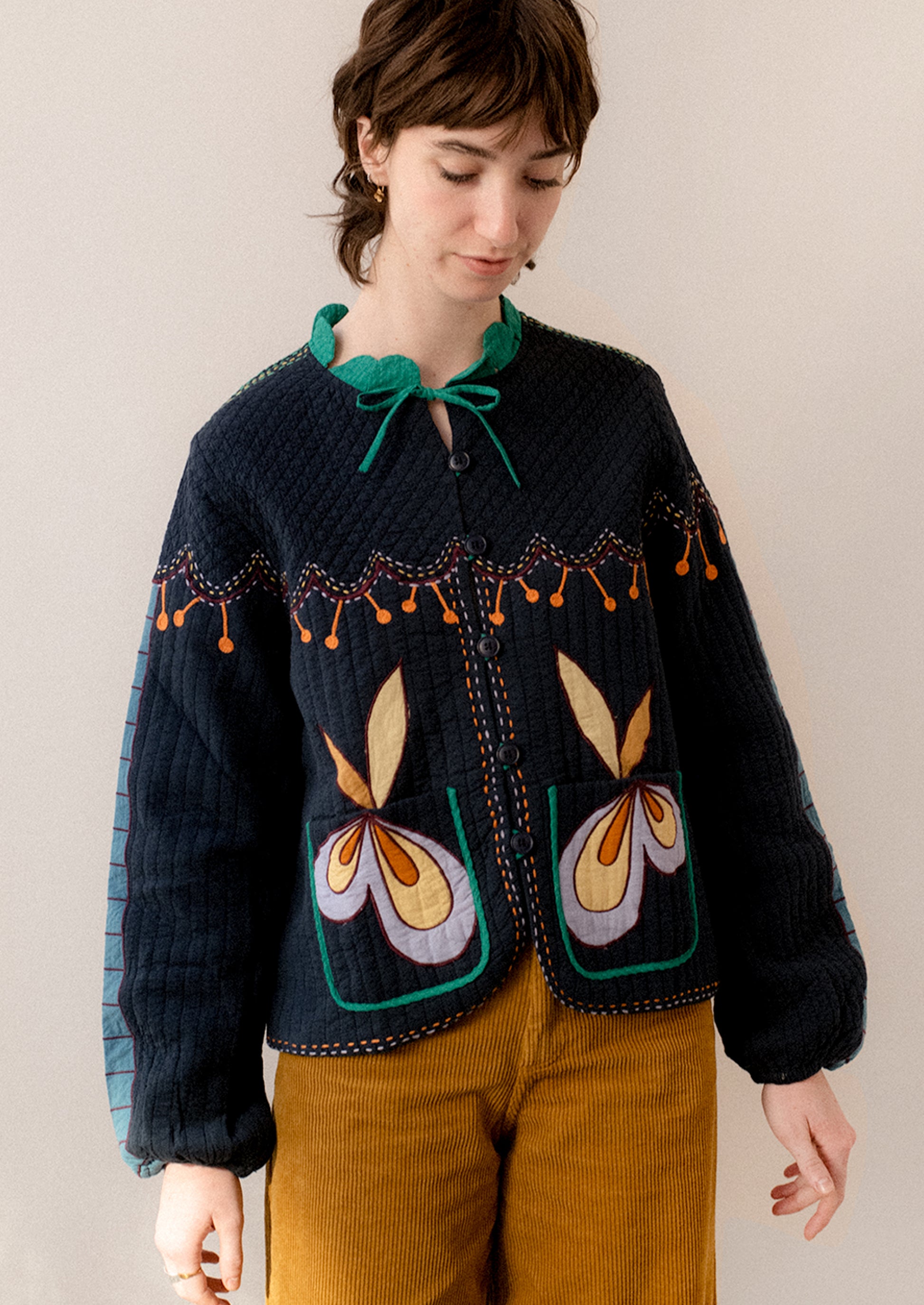 A woman wearing a navy embroidered jacket with whimsical abstract embroidery throughout.