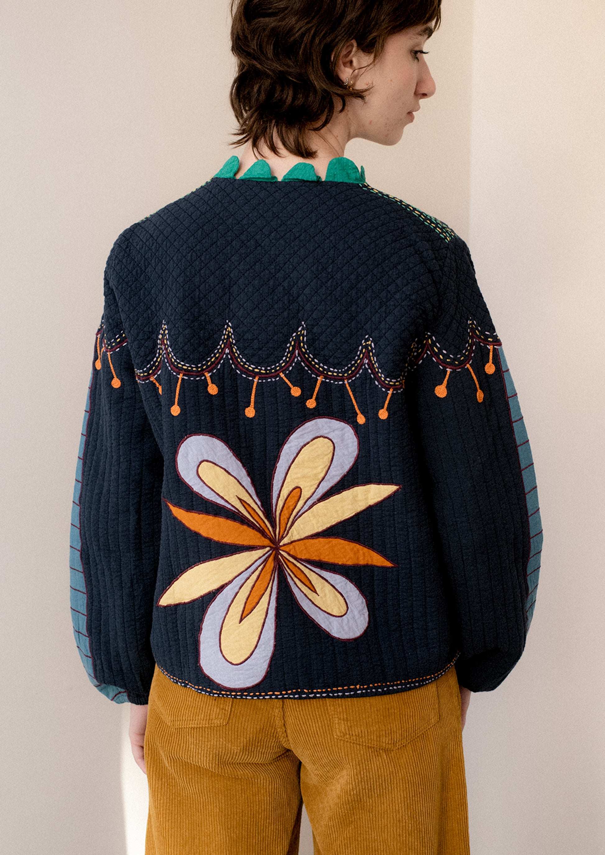 A woman wearing a navy embroidered jacket with whimsical abstract embroidery throughout.