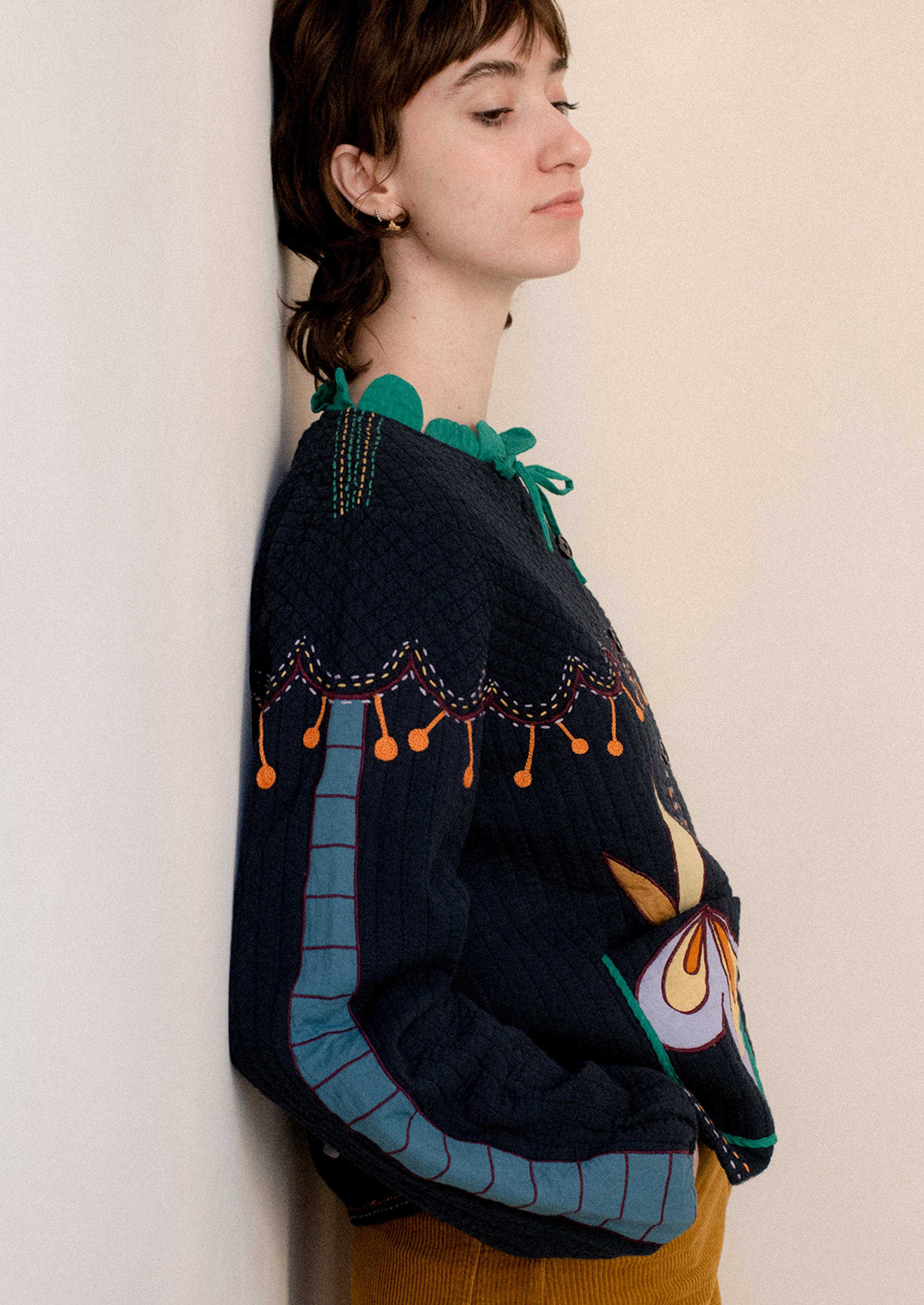 A woman wearing a navy embroidered jacket with whimsical abstract embroidery throughout.