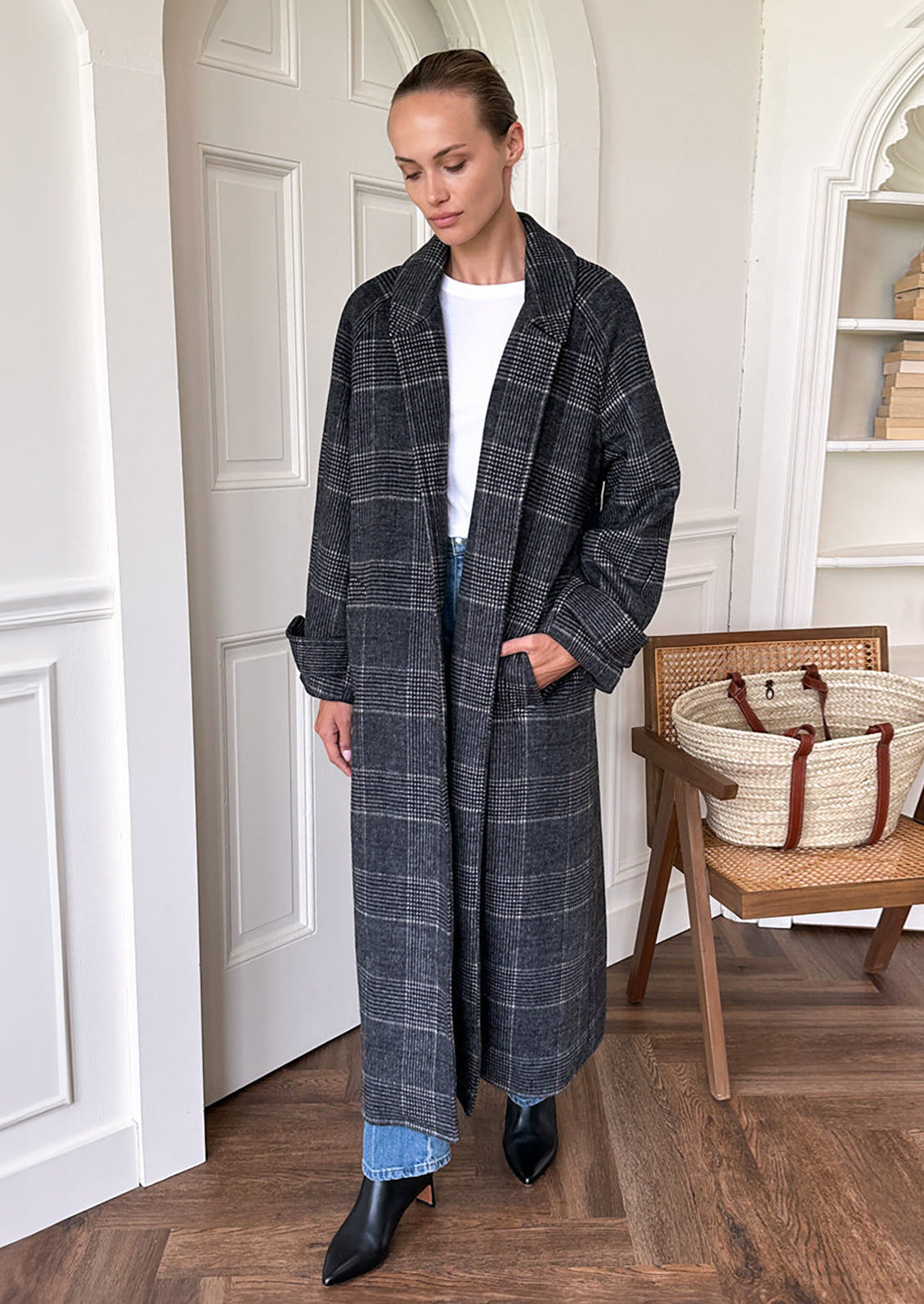 A woman wearing a long wool overcoat in charcoal and white plaid pattern.