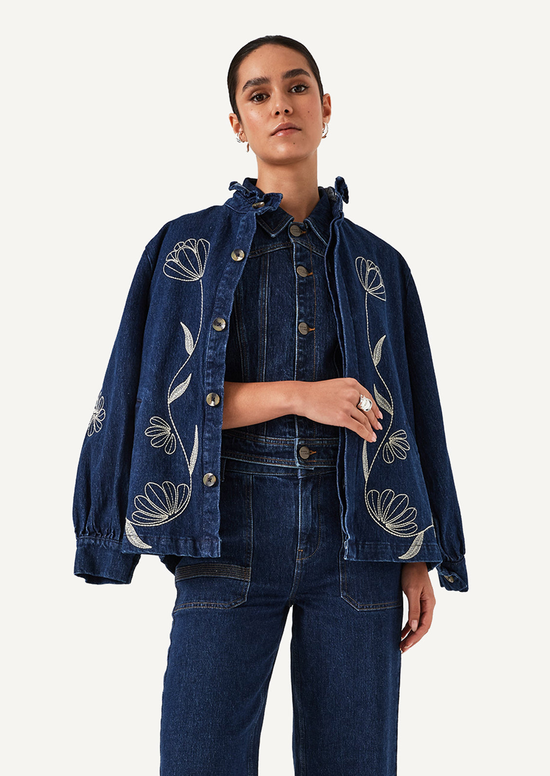 A woman wearing a blue denim jacket with white floral embroidery.