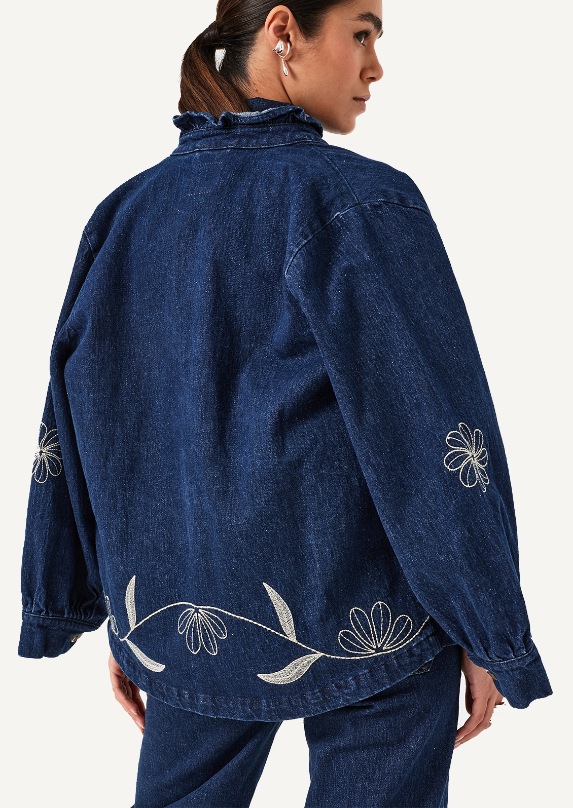 A woman wearing a blue denim jacket with white floral embroidery.