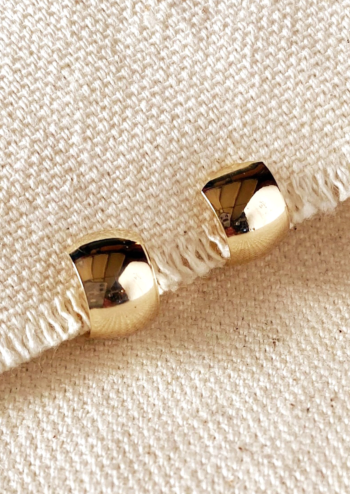 A pair of wide and thick chunky mini hoop earrings with post back in gold.