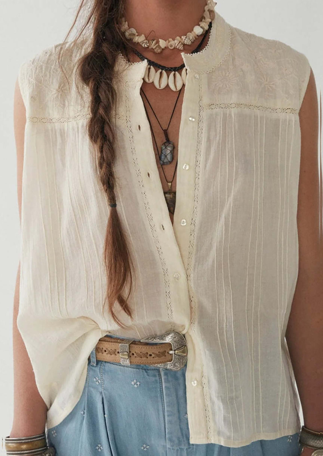A woman wearing a sleeveless cotton button front blouse with tonal embroidered floral pattern at yoke.