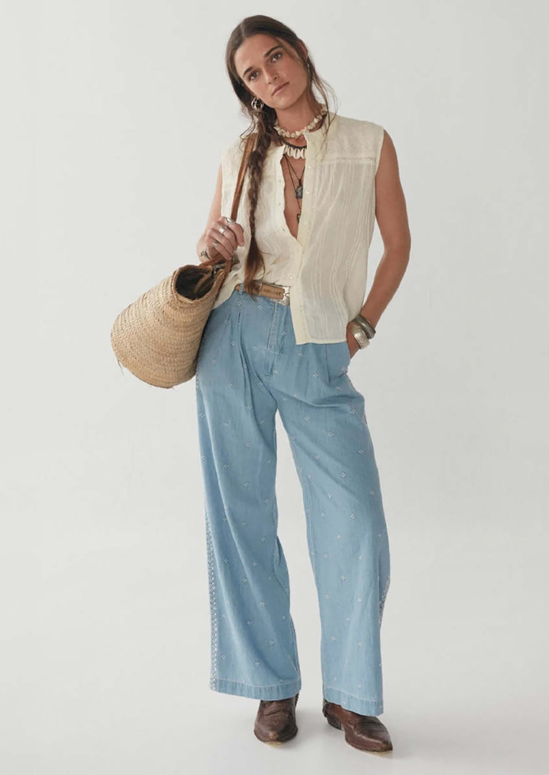 A woman wearing a sleeveless cotton button front blouse with tonal embroidered floral pattern at yoke.
