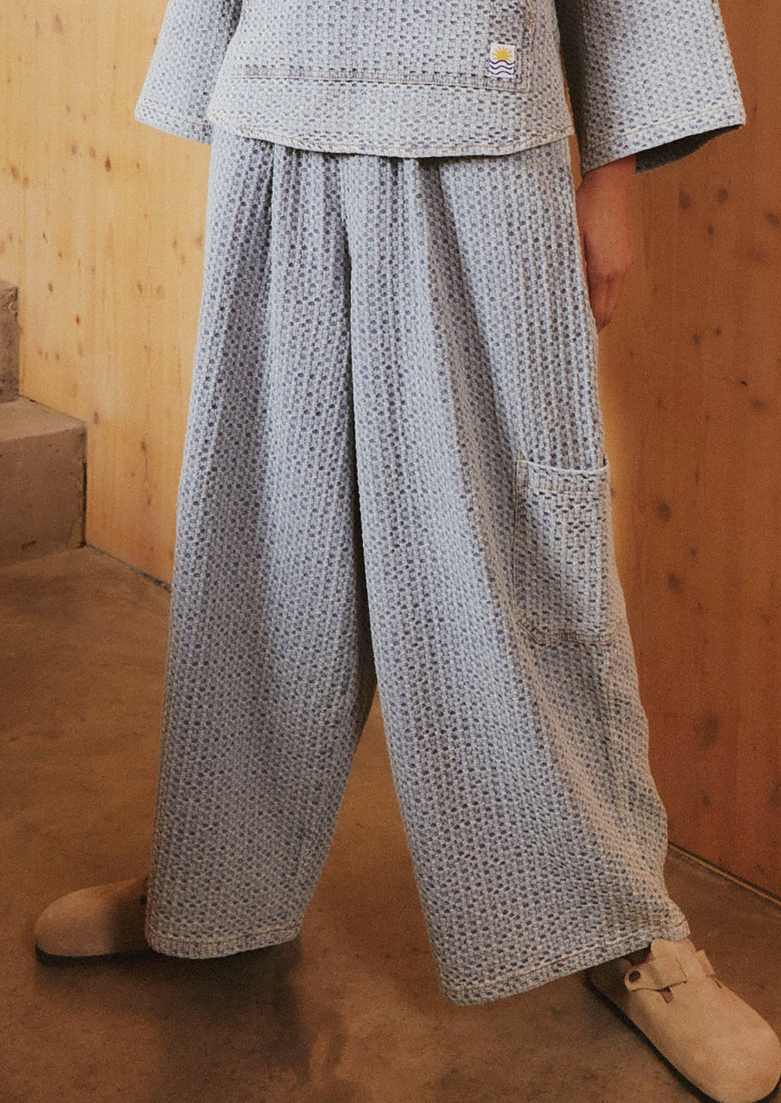 A woman wearing a pair of wide leg, seersucker texture pants in light blue.