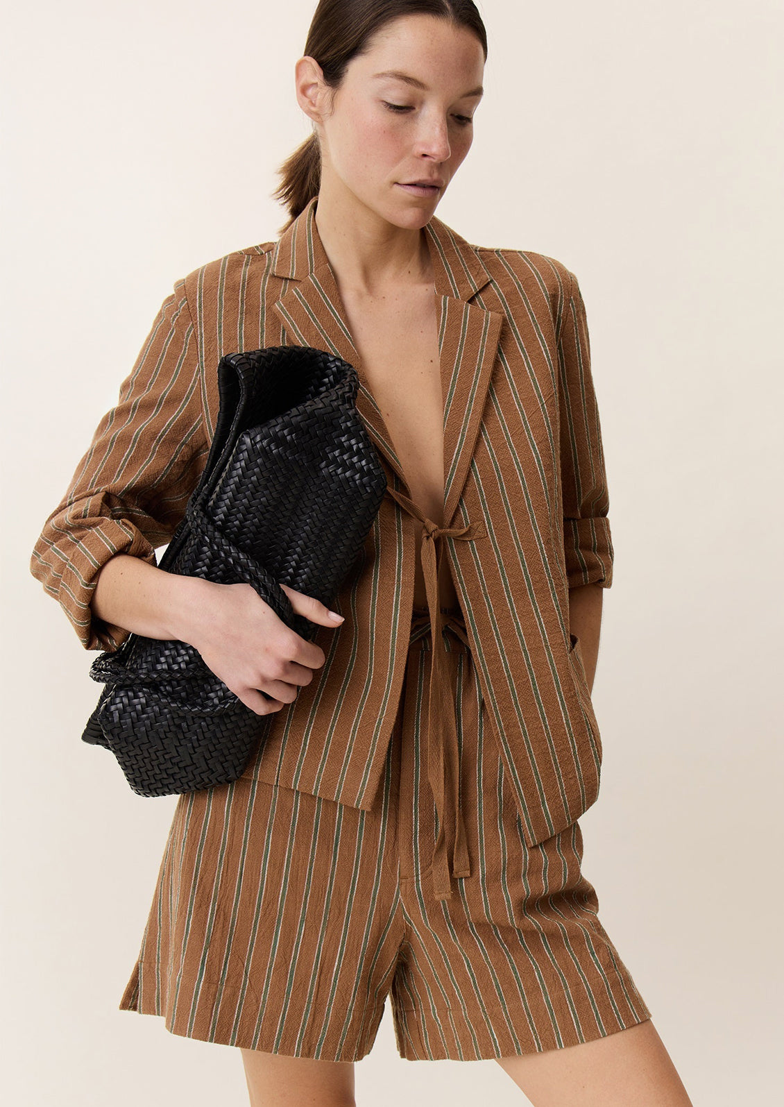 A person wearing a pair of tailored shorts in brown with green stripe pattern.