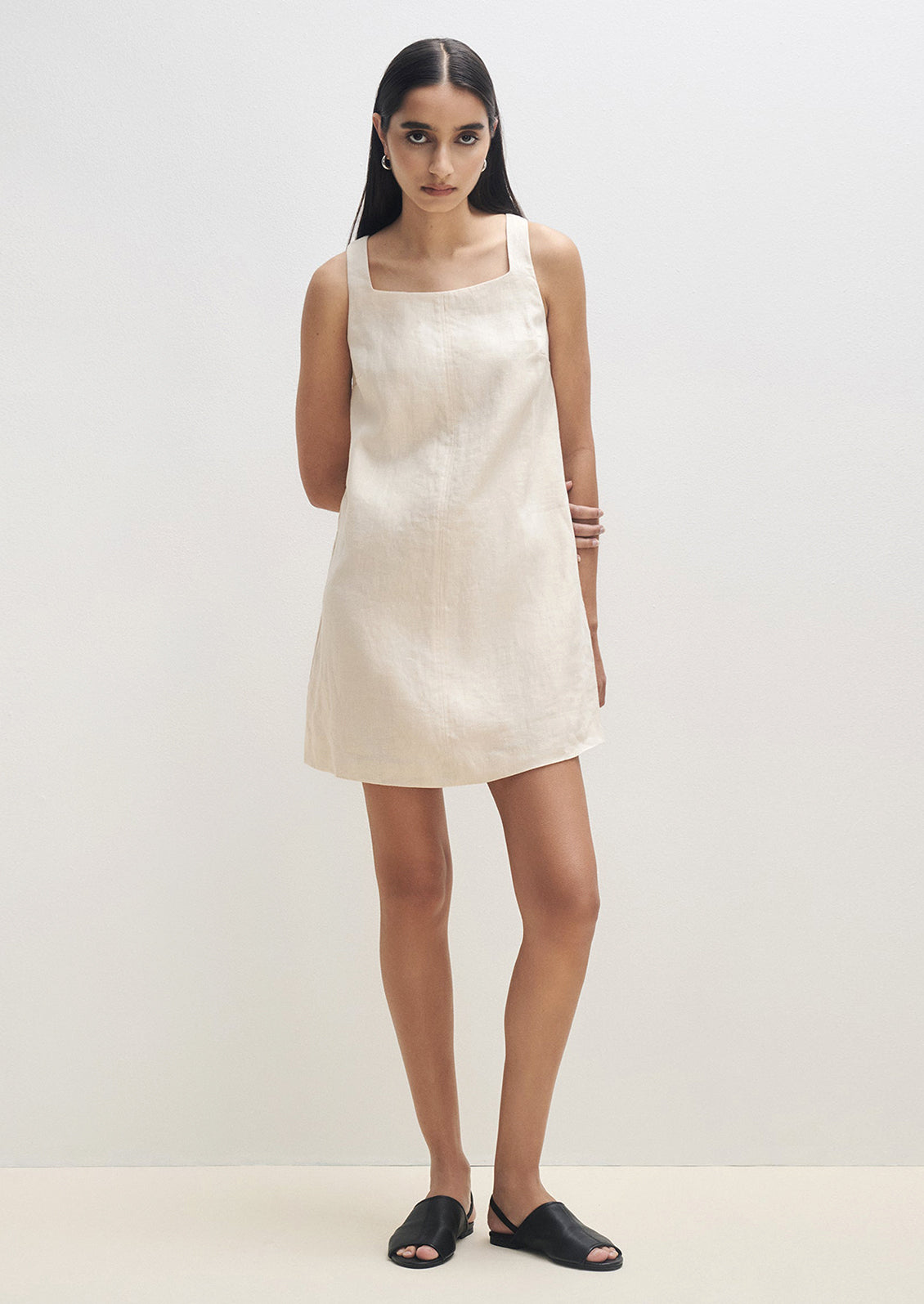 A woman wearing a natural colored linen mini dress with square neck.
