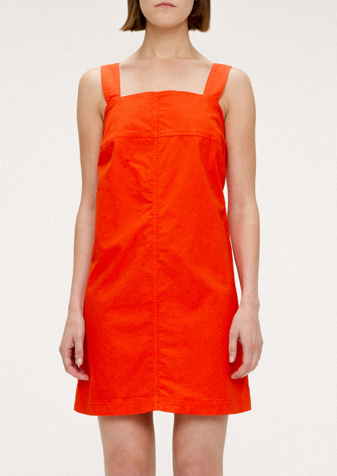 A woman wearing a short red-orange dress with square neckline and wide shoulder straps.
