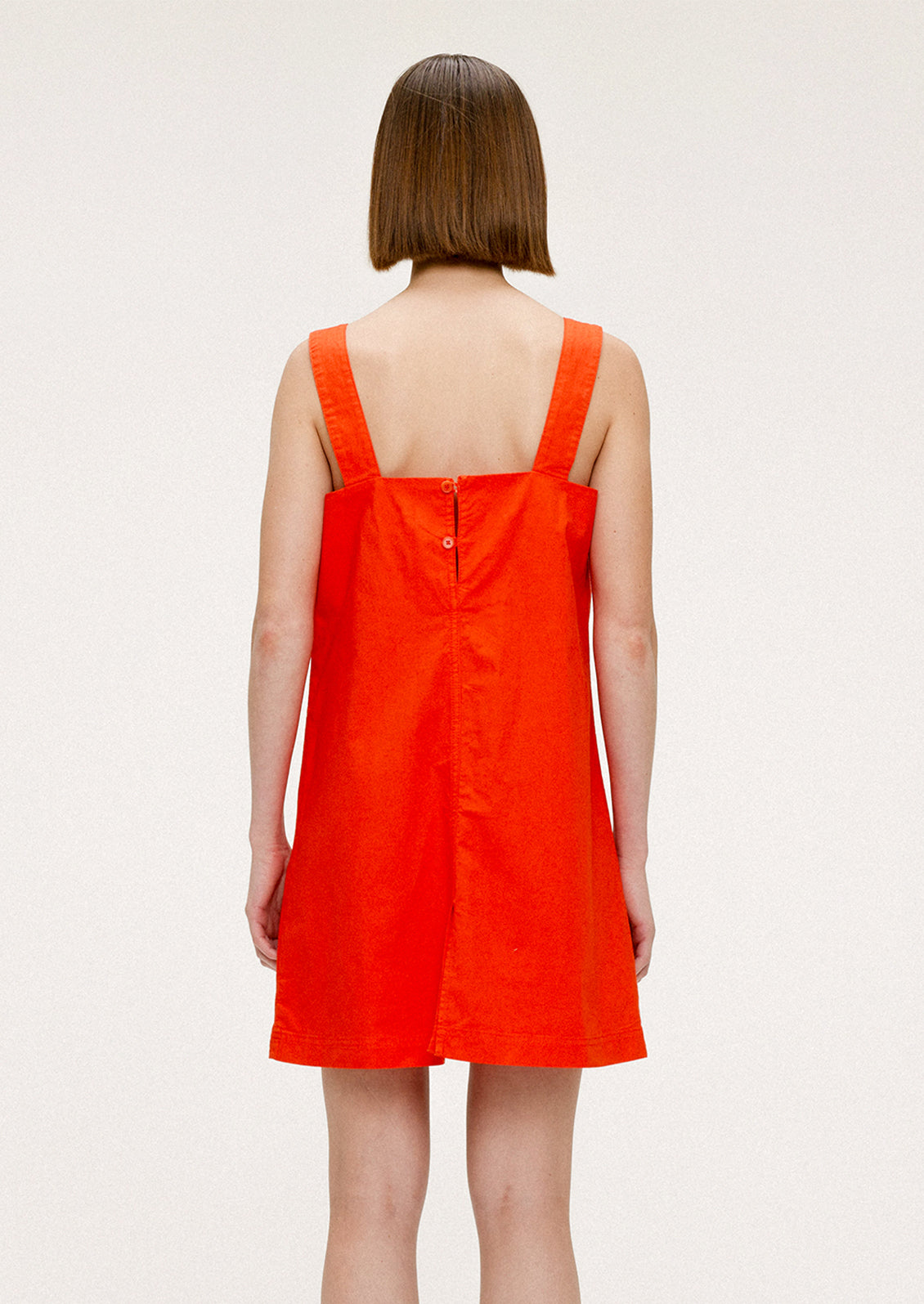 A woman wearing a short red-orange dress with square neckline and wide shoulder straps.