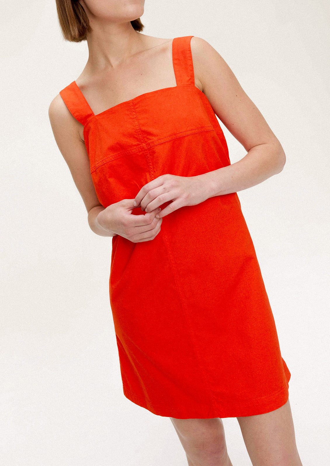 A woman wearing a short red-orange dress with square neckline and wide shoulder straps.
