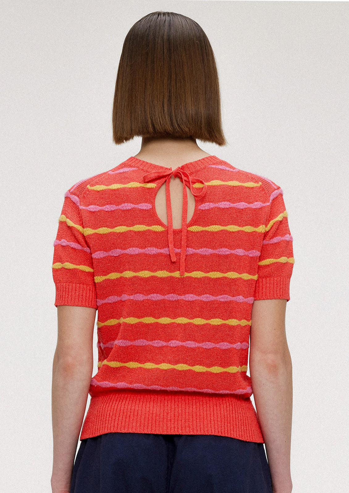 A woman wearing a red short sleeve knit top with yellow and pink wavy stripes.