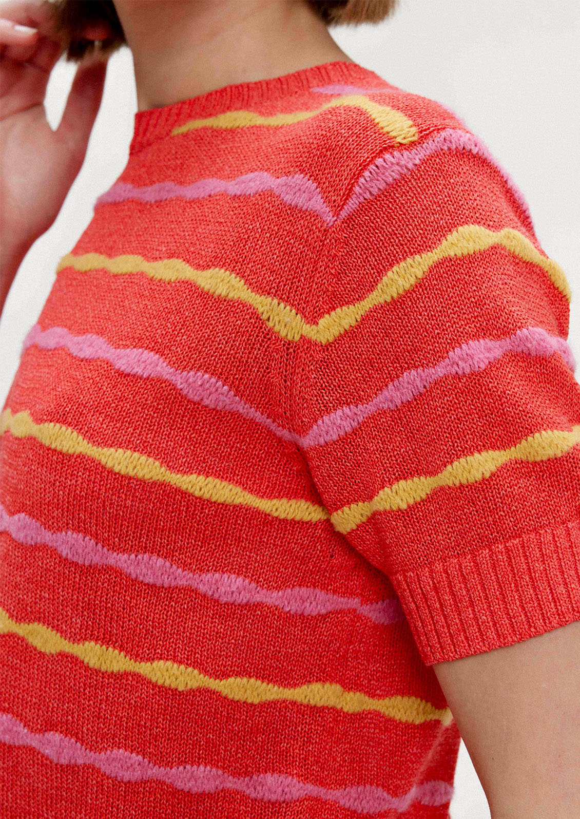 A woman wearing a red short sleeve knit top with yellow and pink wavy stripes.