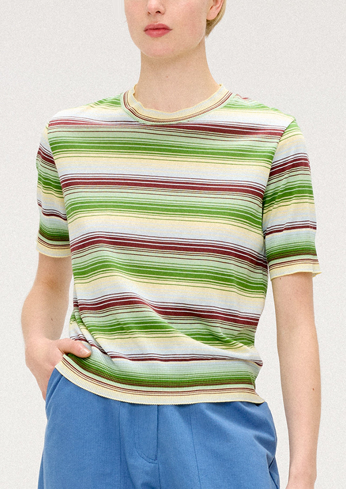 A person wearing a knit t-shirt with multi stripe pattern in green, cream and brown.