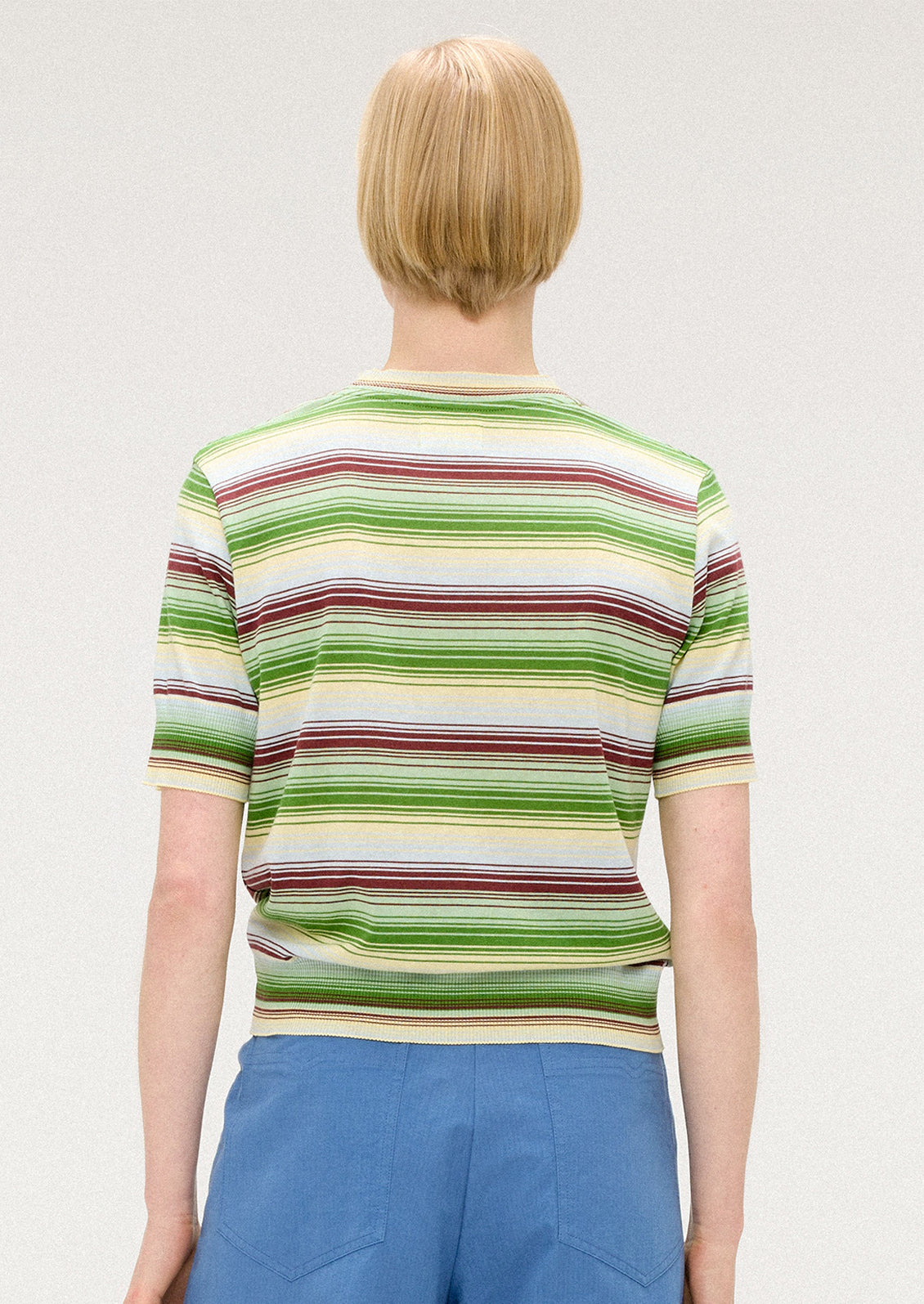 A person wearing a knit t-shirt with multi stripe pattern in green, cream and brown.