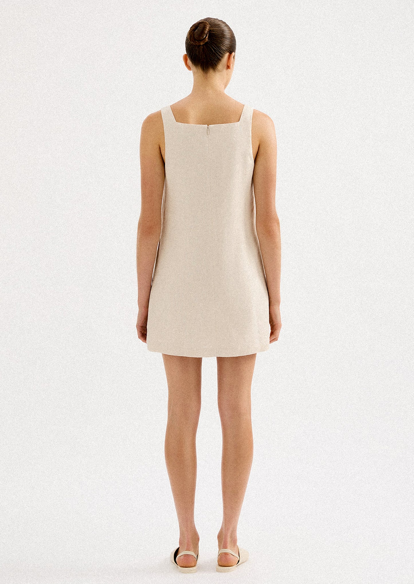 A woman wearing a natural colored linen mini dress with square neck.