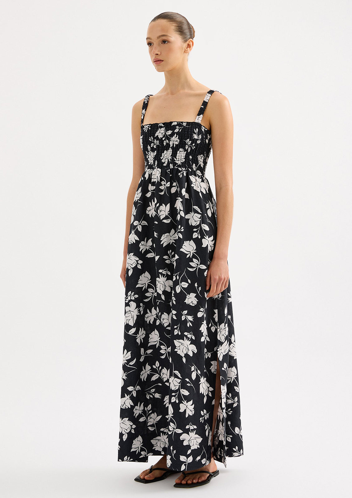 A woman wearing a black and white floral print maxi dress with smocked bodice.