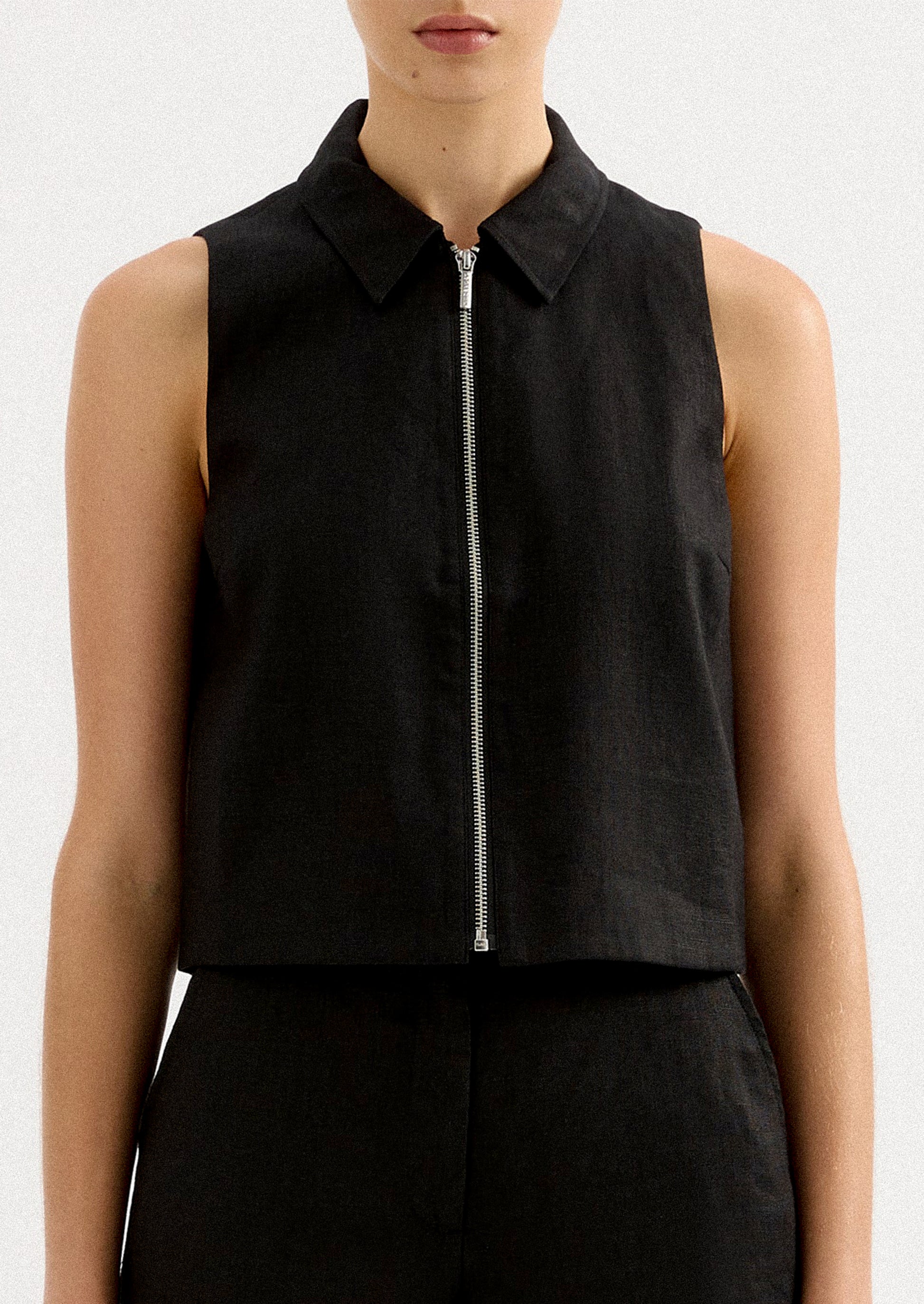 A woman wearing a sleeveless collared shirt with full length silver zipper at front placket.