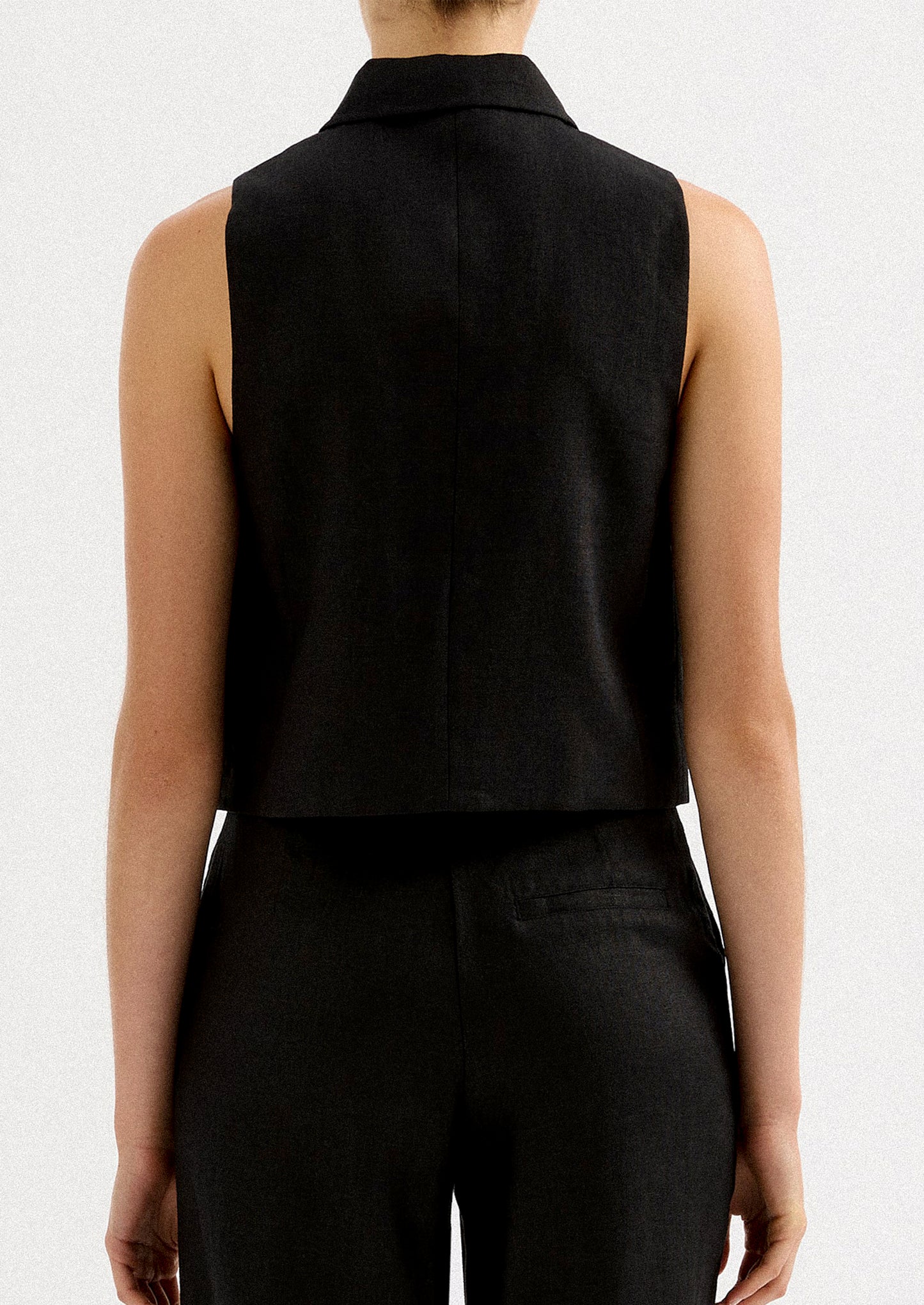 A woman wearing a sleeveless collared shirt with full length silver zipper at front placket.