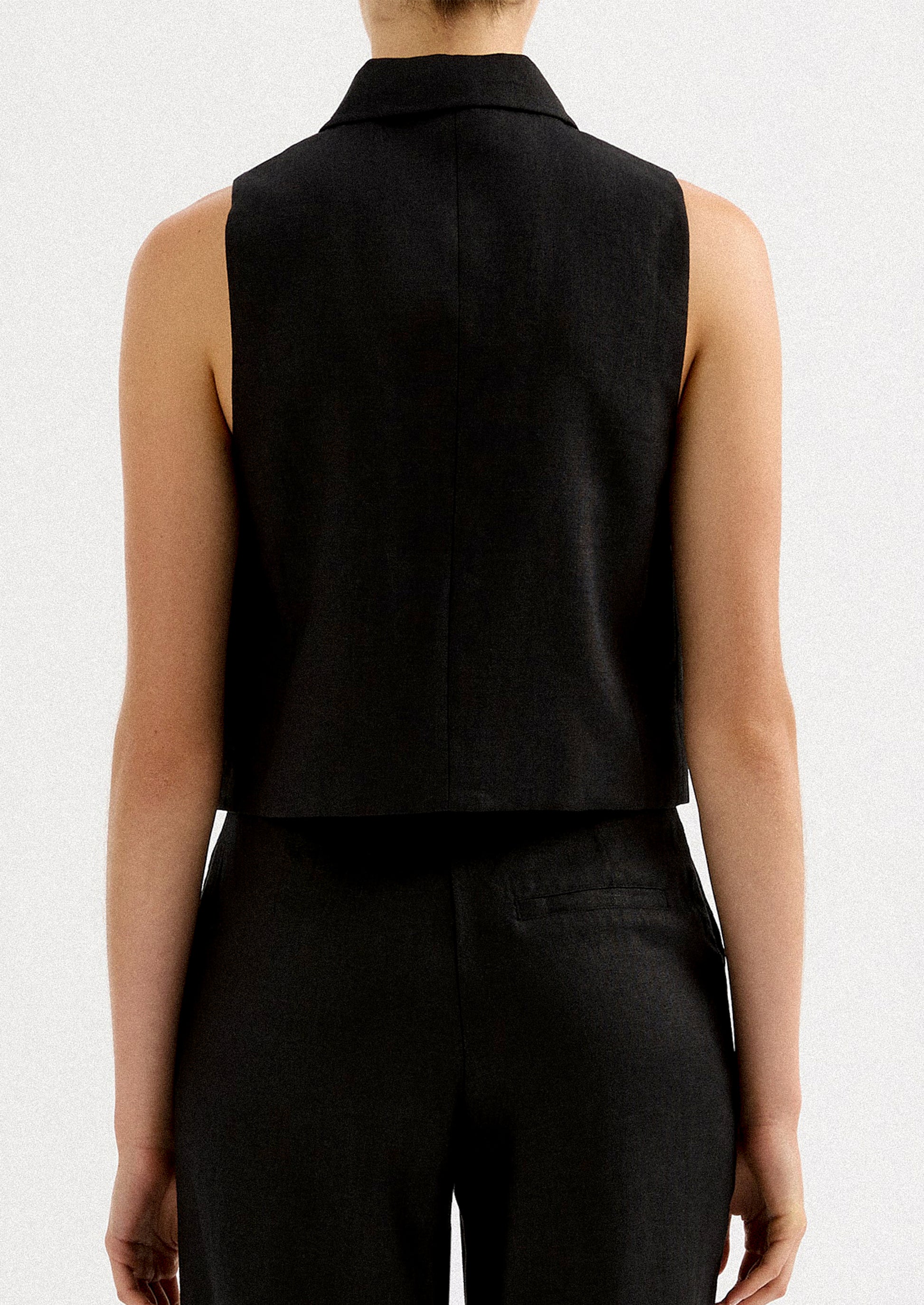 A woman wearing a sleeveless collared shirt with full length silver zipper at front placket.