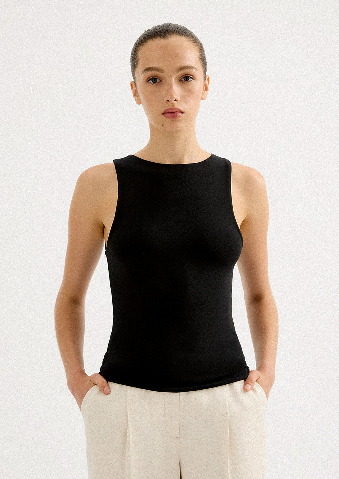 A woman wearing a solid black sleeveless tank top with high round neckline.
