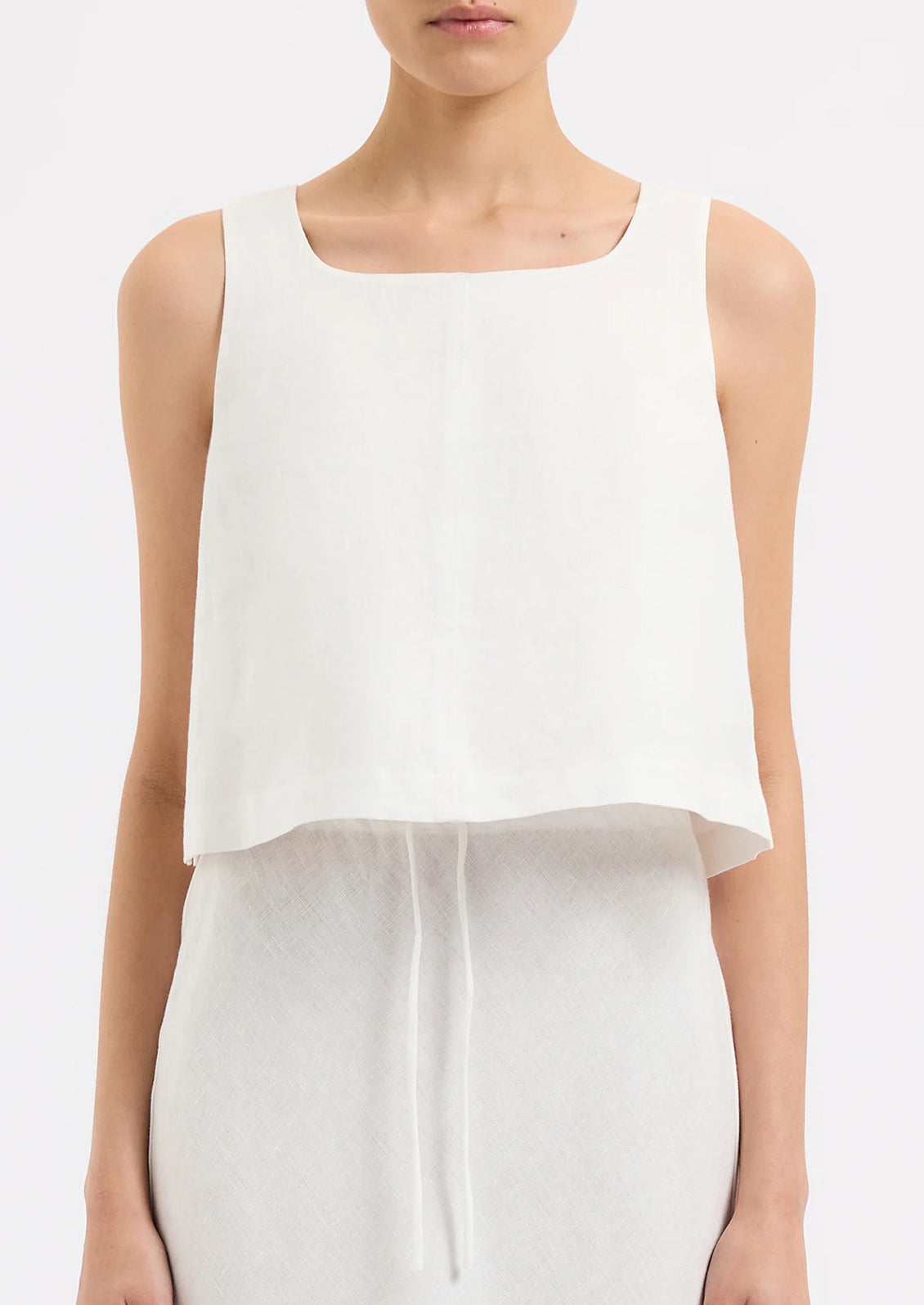A person wearing a sleeveless shift tank in white.