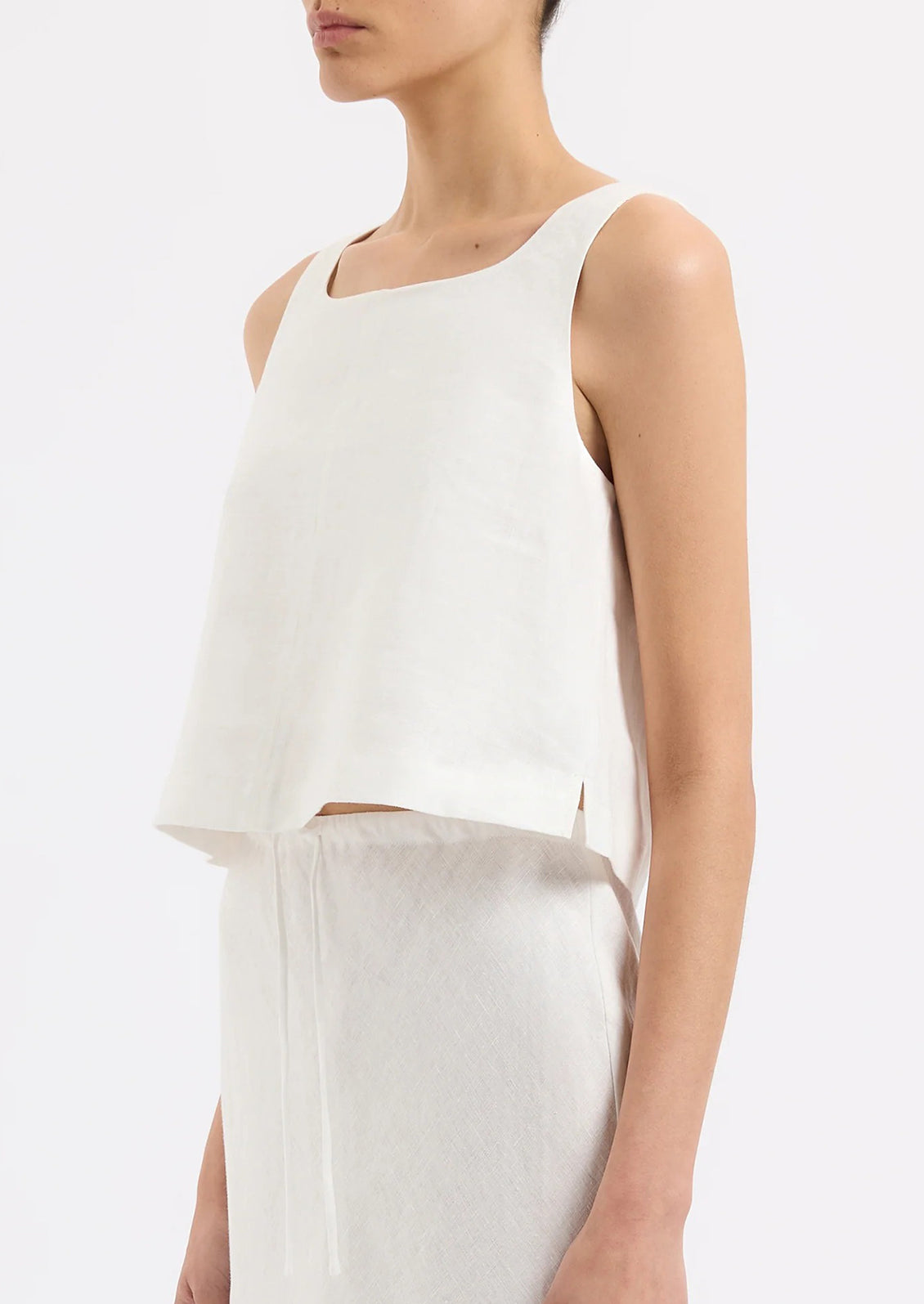 A person wearing a sleeveless shift tank in white.