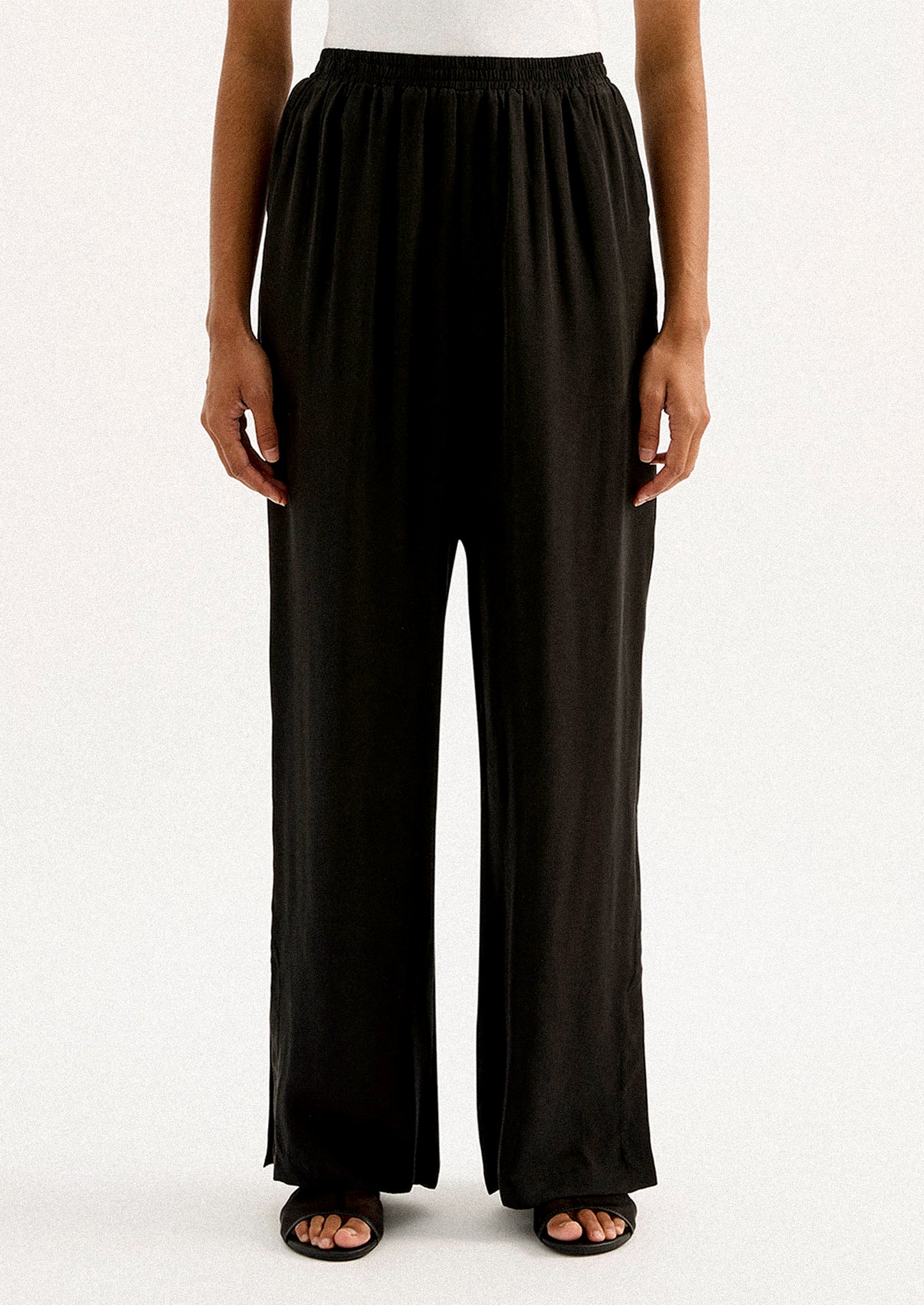 A person wearing a pair of black sateen pants with split leg hem.