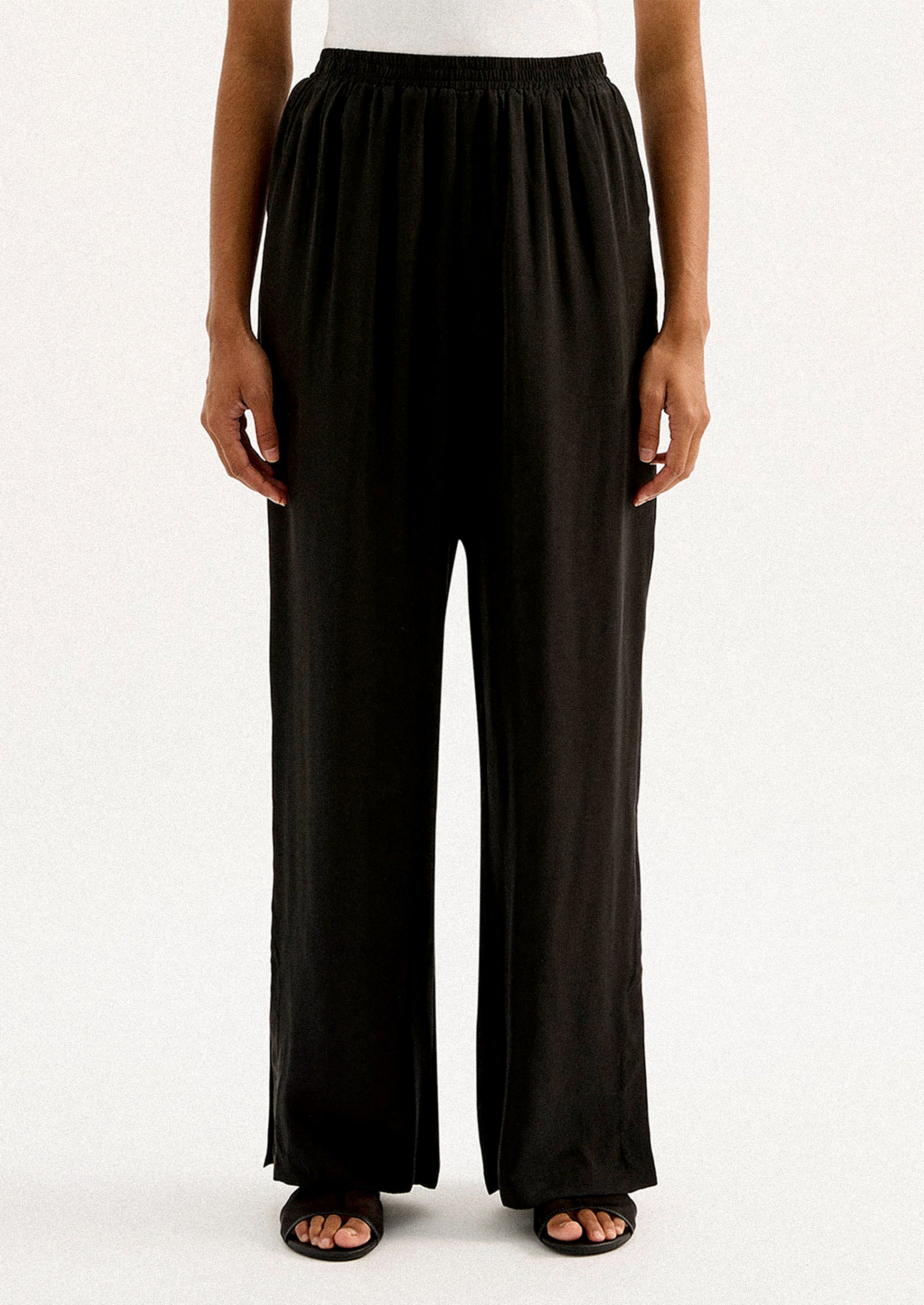 A person wearing a pair of black sateen pants with split leg hem.