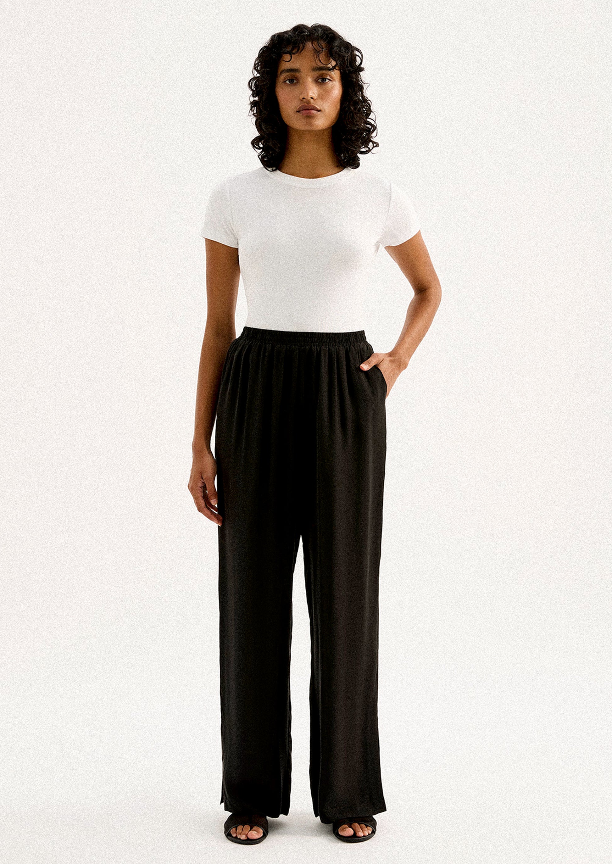 A person wearing a pair of black sateen pants with split leg hem.