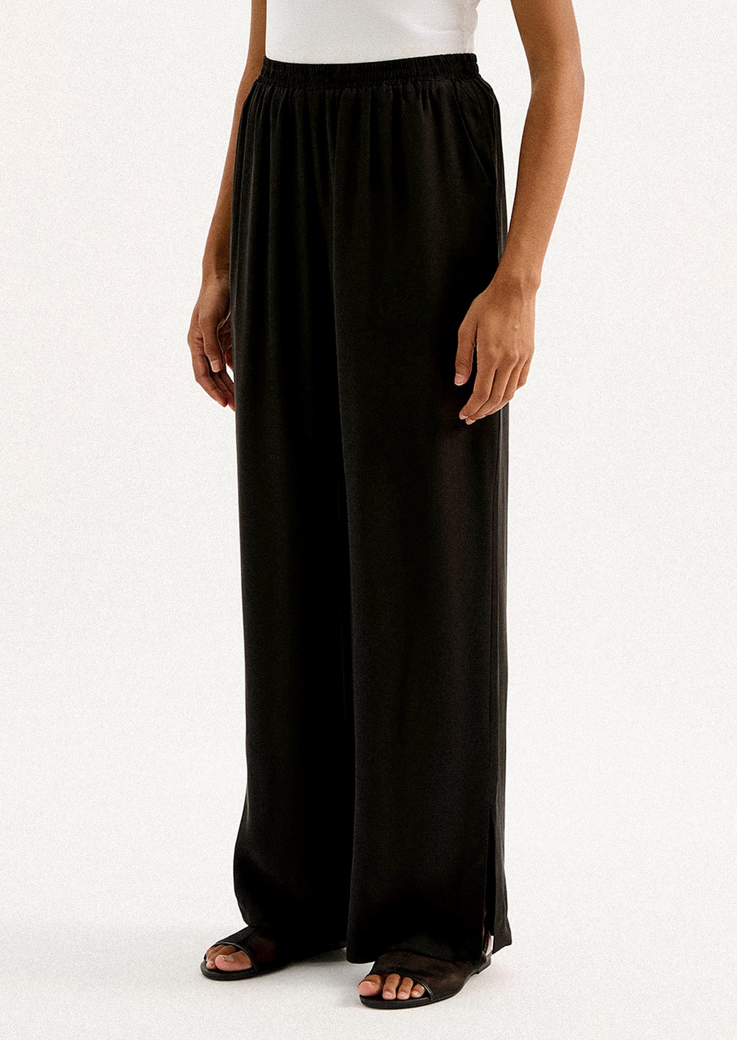 A person wearing a pair of black sateen pants with split leg hem.