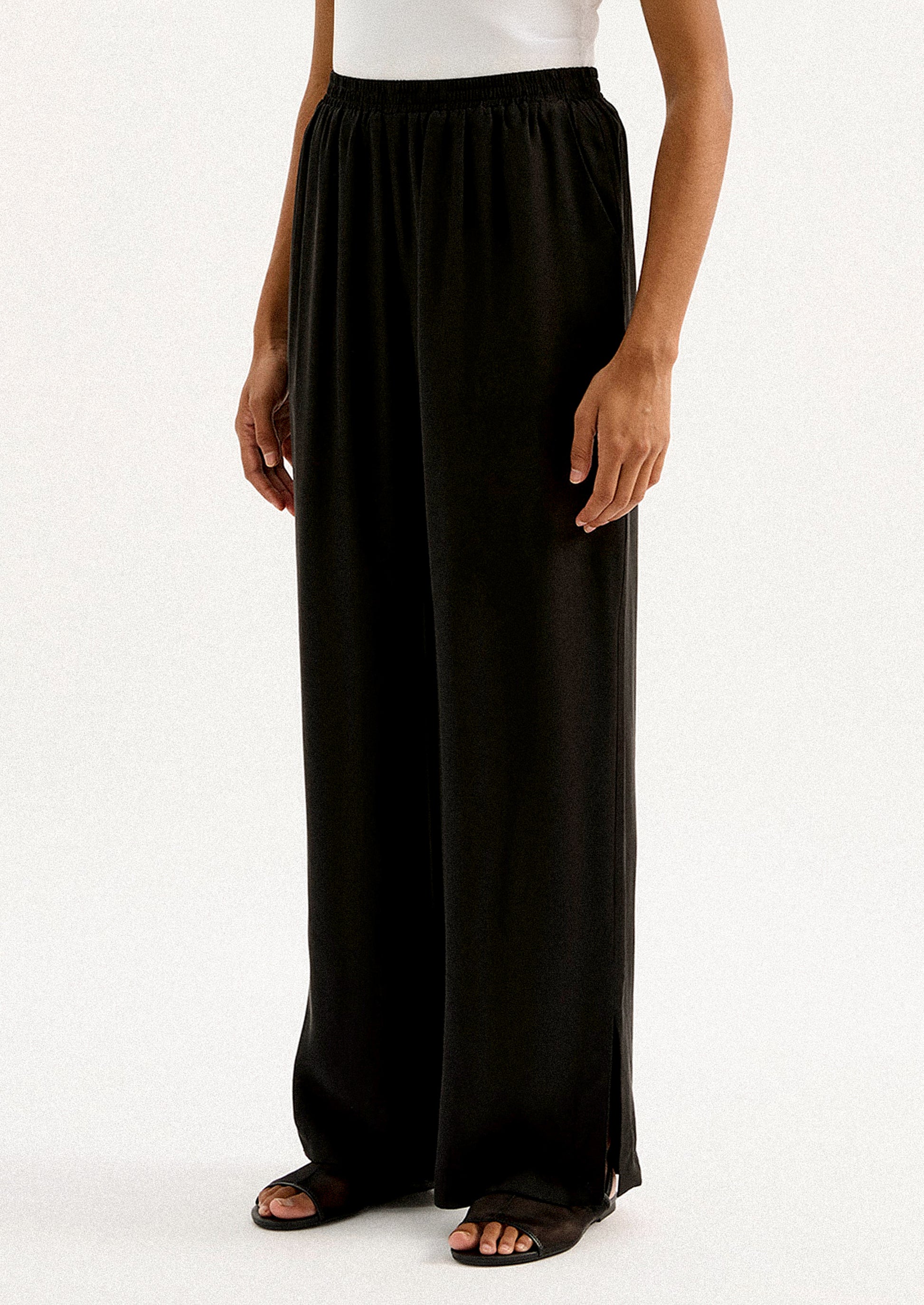 A person wearing a pair of black sateen pants with split leg hem.