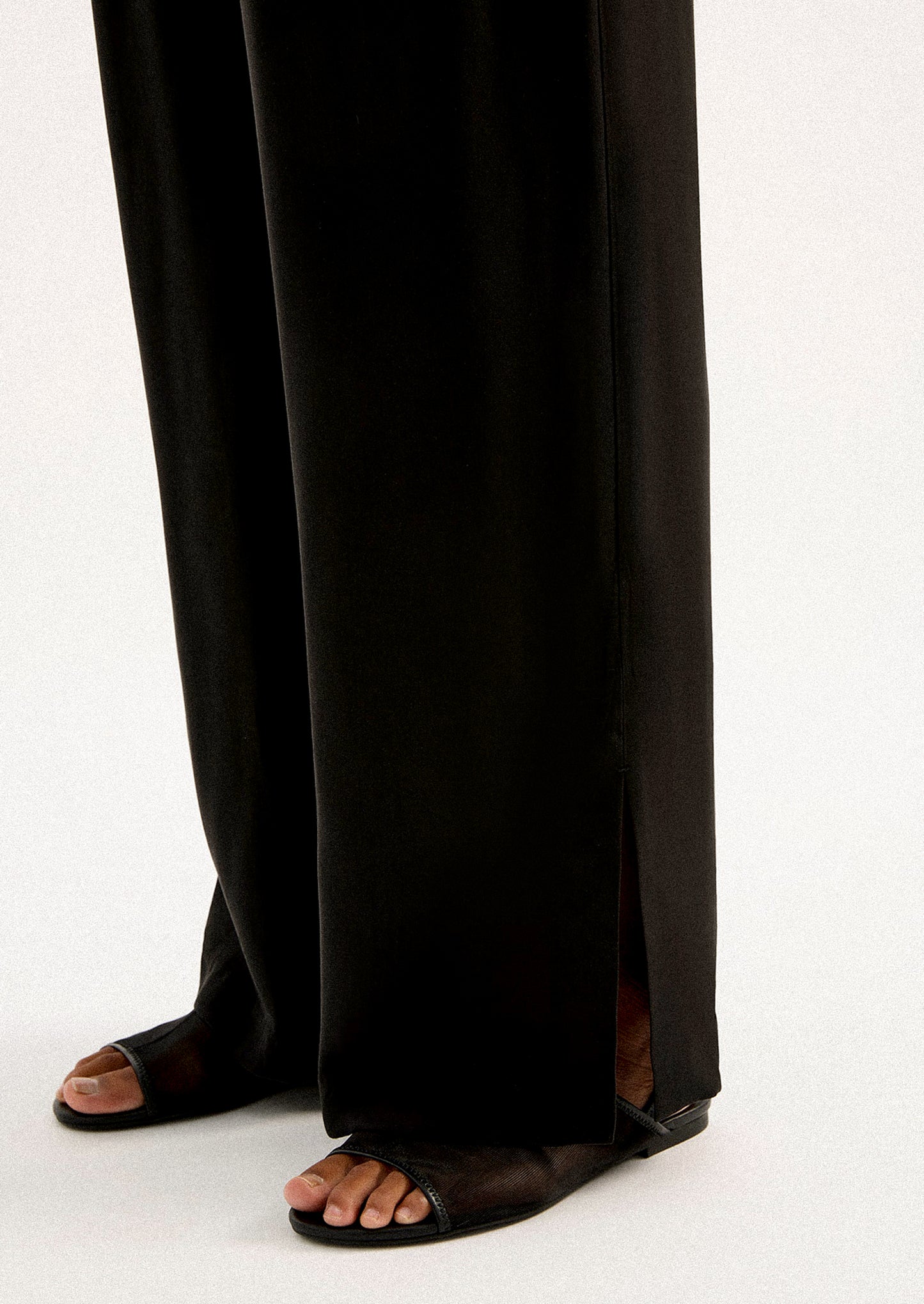 A person wearing a pair of black sateen pants with split leg hem.
